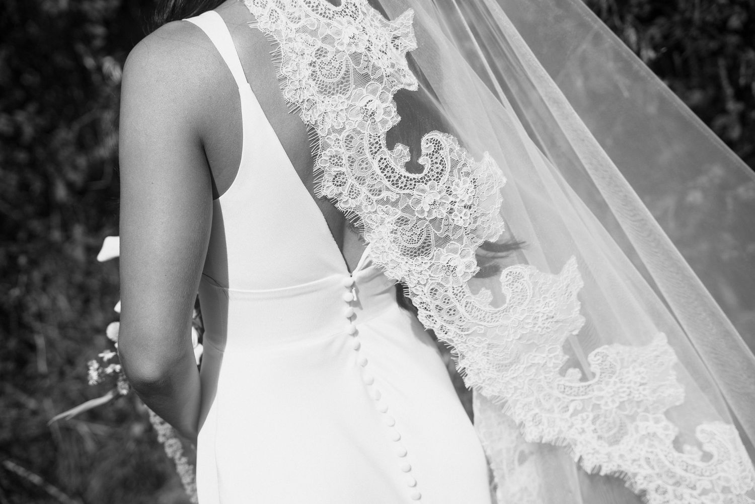 Black and white photo of a bride in a sleeveless gown with lace veil and button back detail.