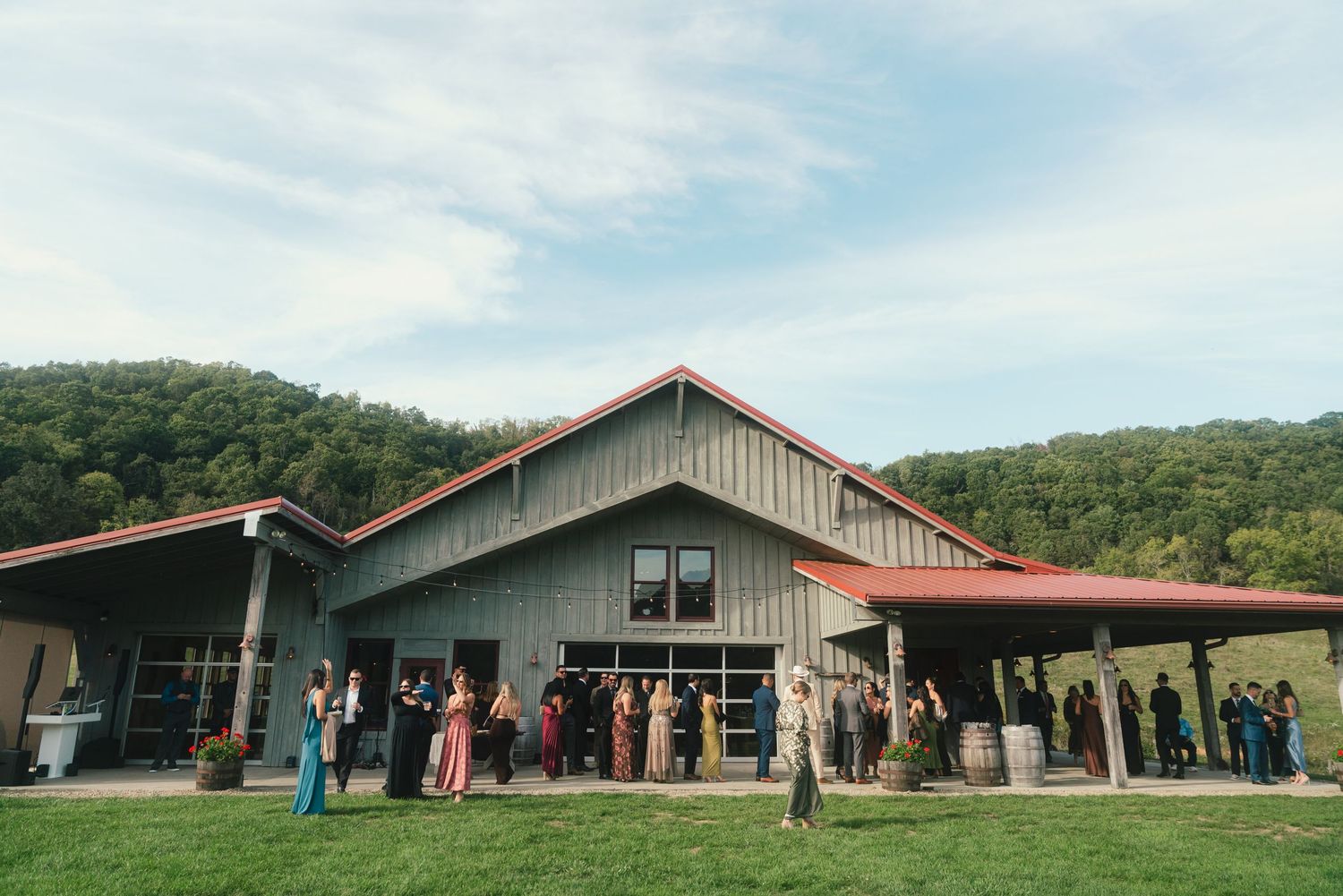 Rustic barn wedding venue with red roof set against rolling green hills in Weaverville, NC, with guests gathered outside.