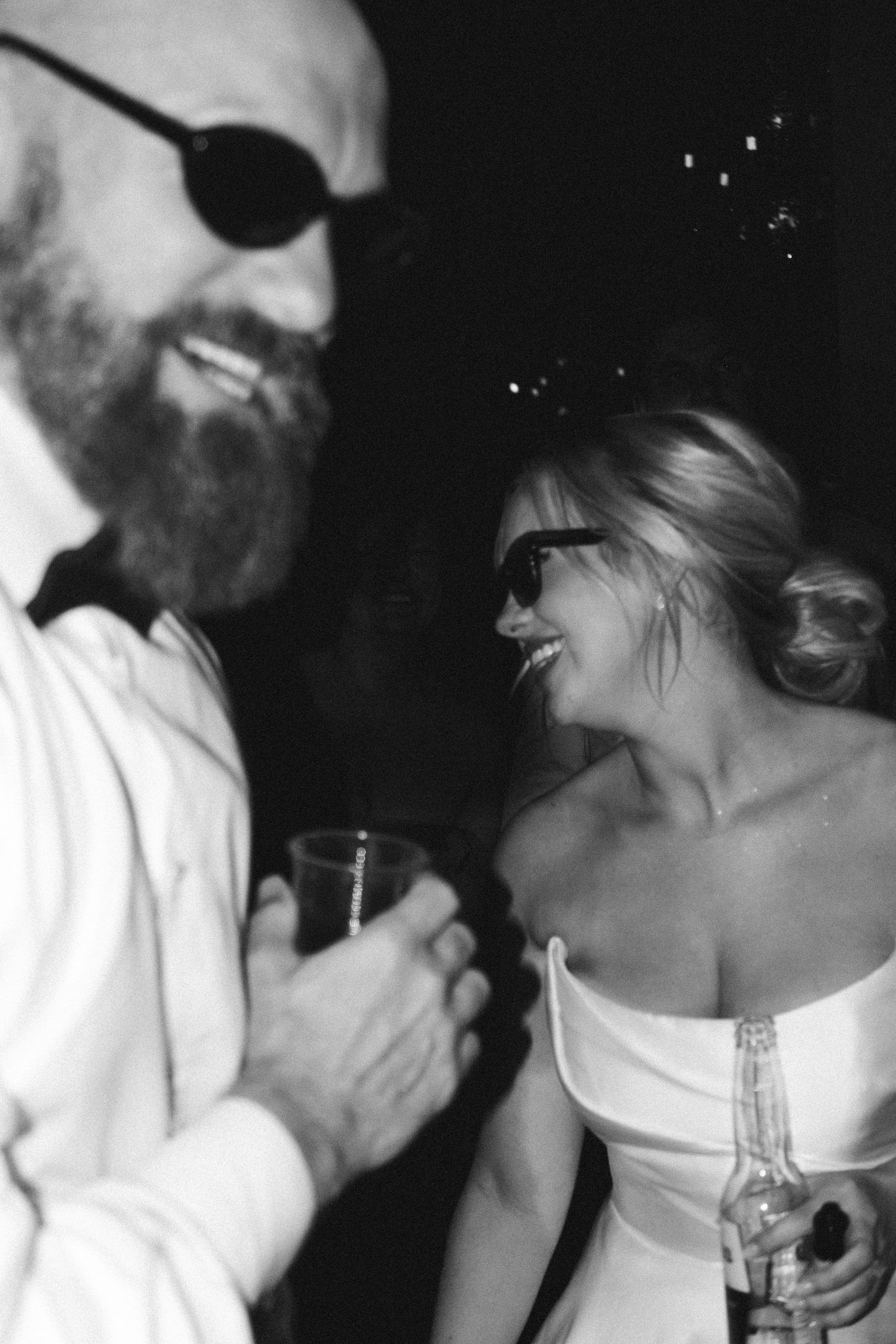 A couple wearing sunglasses share a candid moment at their wedding reception.