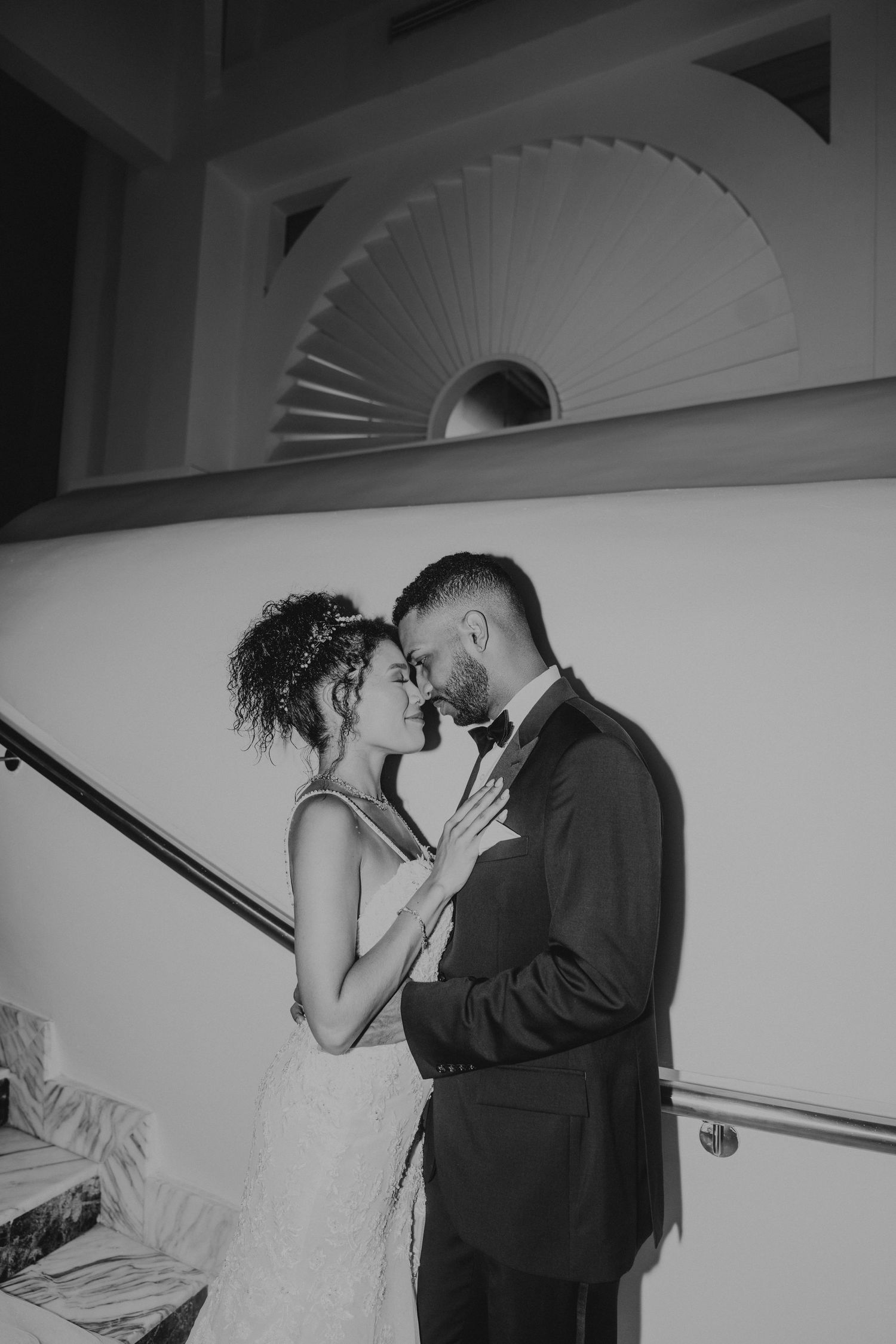 Romantic black and white photo of a couple under a decorative fan archway.