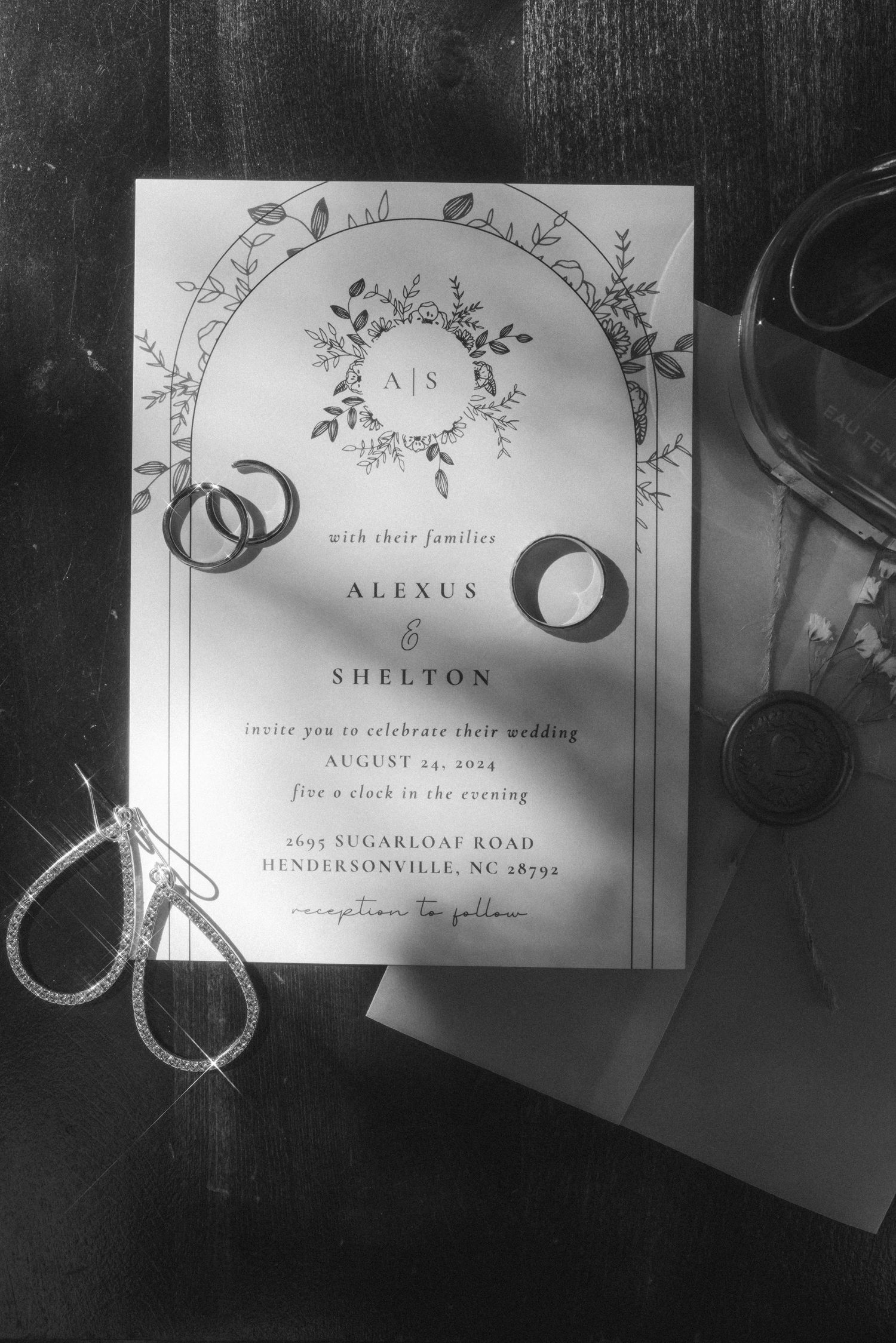 Black and white photo of wedding invitation with rings and floral design.