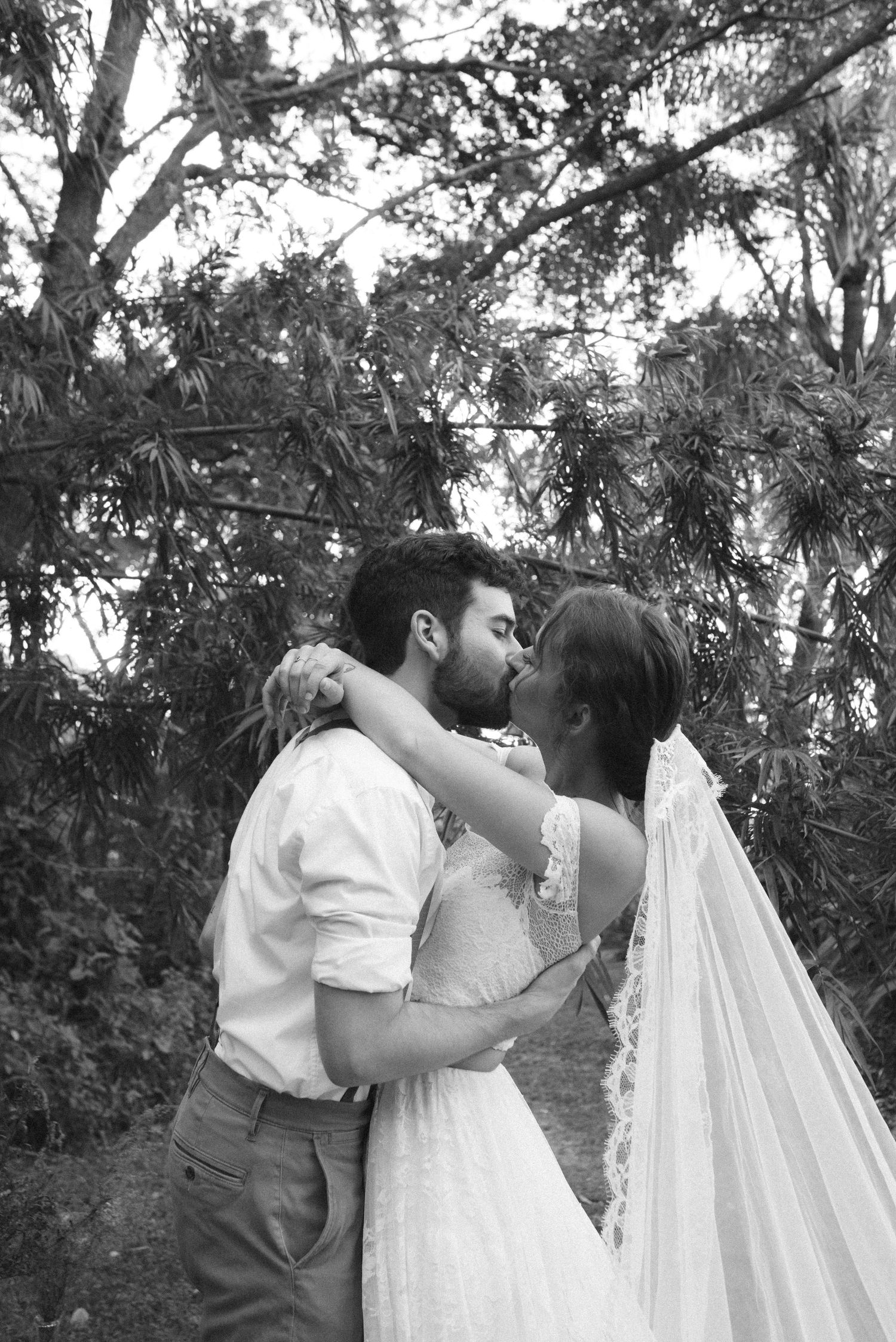 Romantic black and white portrait of newlyweds embracing under tree branches.