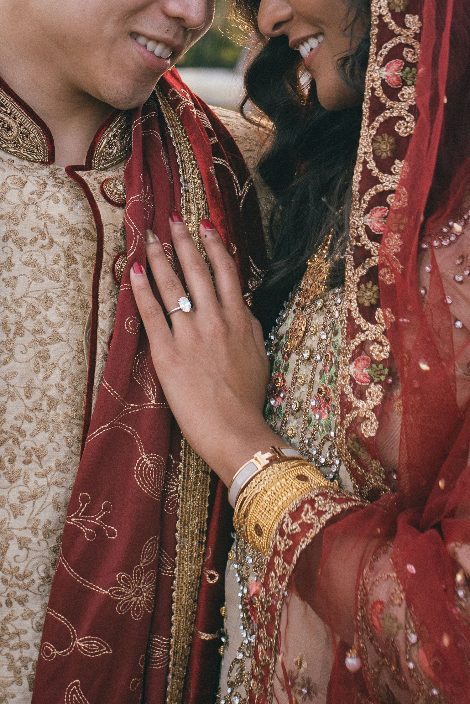 Close-up of hands showing engagement ring and traditional South Asian wedding attire with intricate embroidery and jewelry.