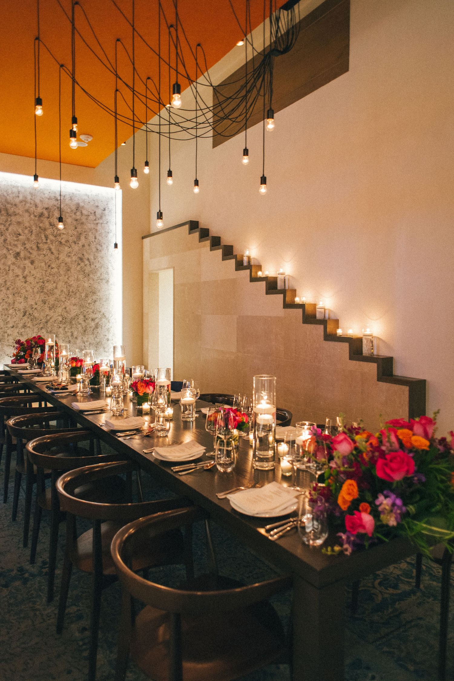 Modern wedding reception table setting with hanging pendant lights and colorful floral arrangements.