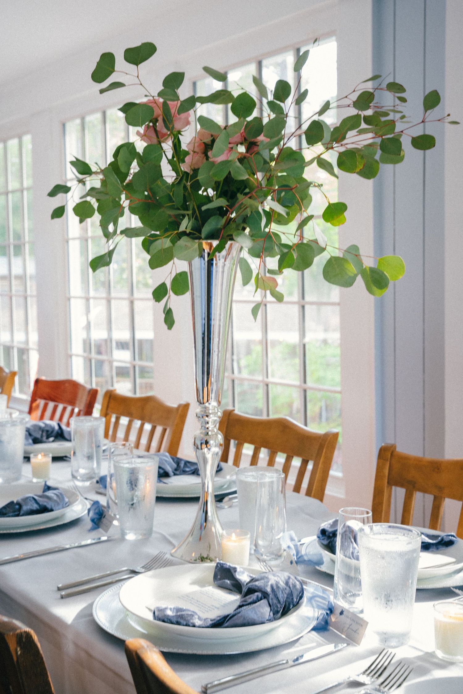 Elegant wedding reception table setting with eucalyptus centerpieces and blue napkins.