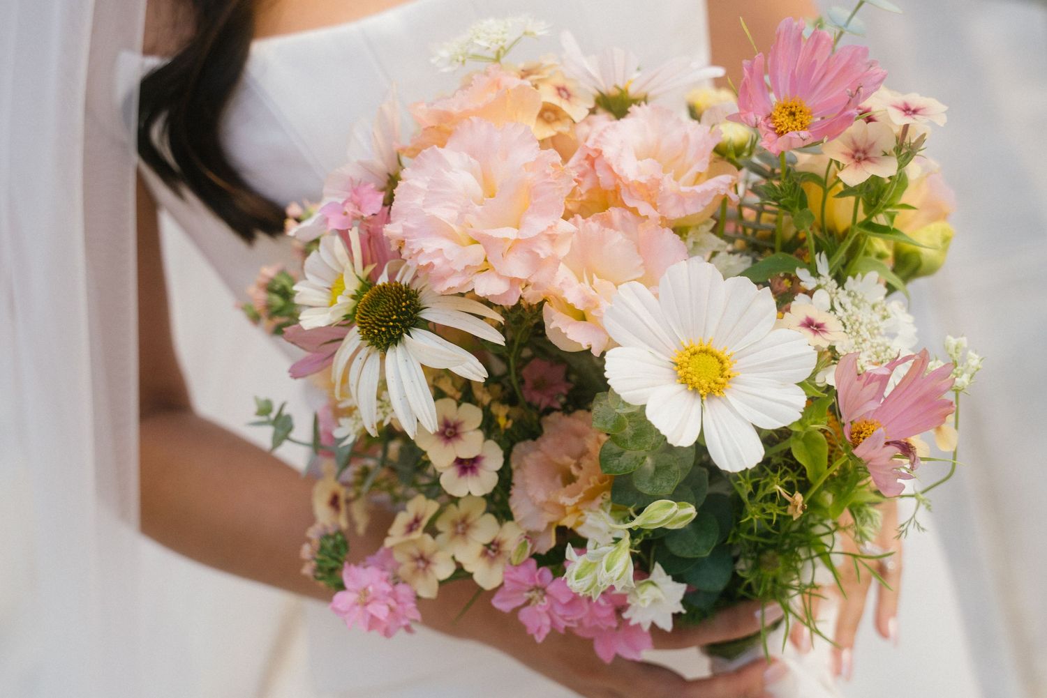Bride holding a beautiful bouquet of pink peonies, white daisies, and wildflowers on her wedding day.