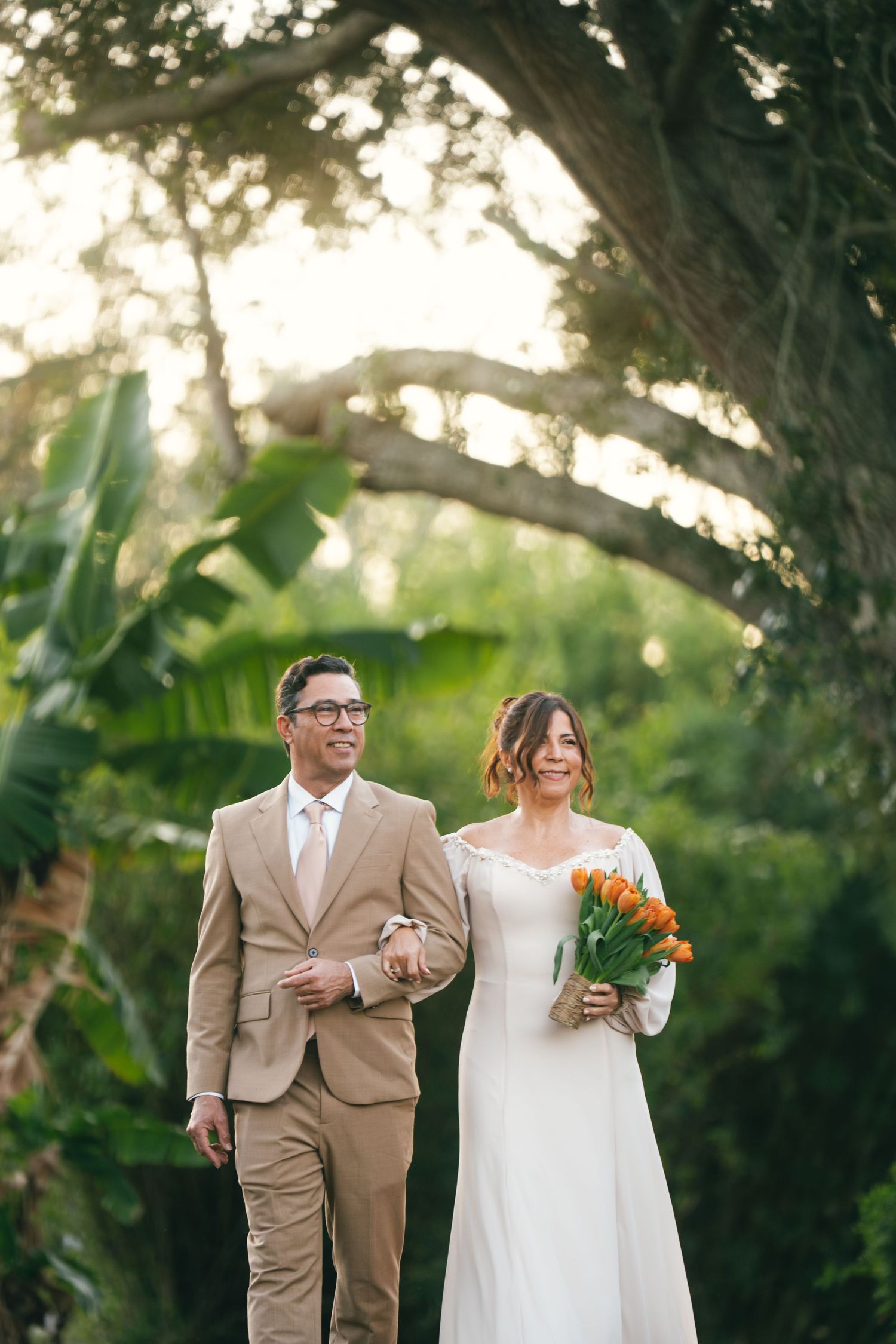 Wedding couple poses under large tree branches during golden hour.