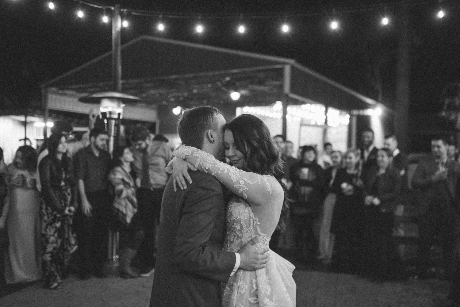 A couple shares their first dance at their wedding reception under hanging string lights.