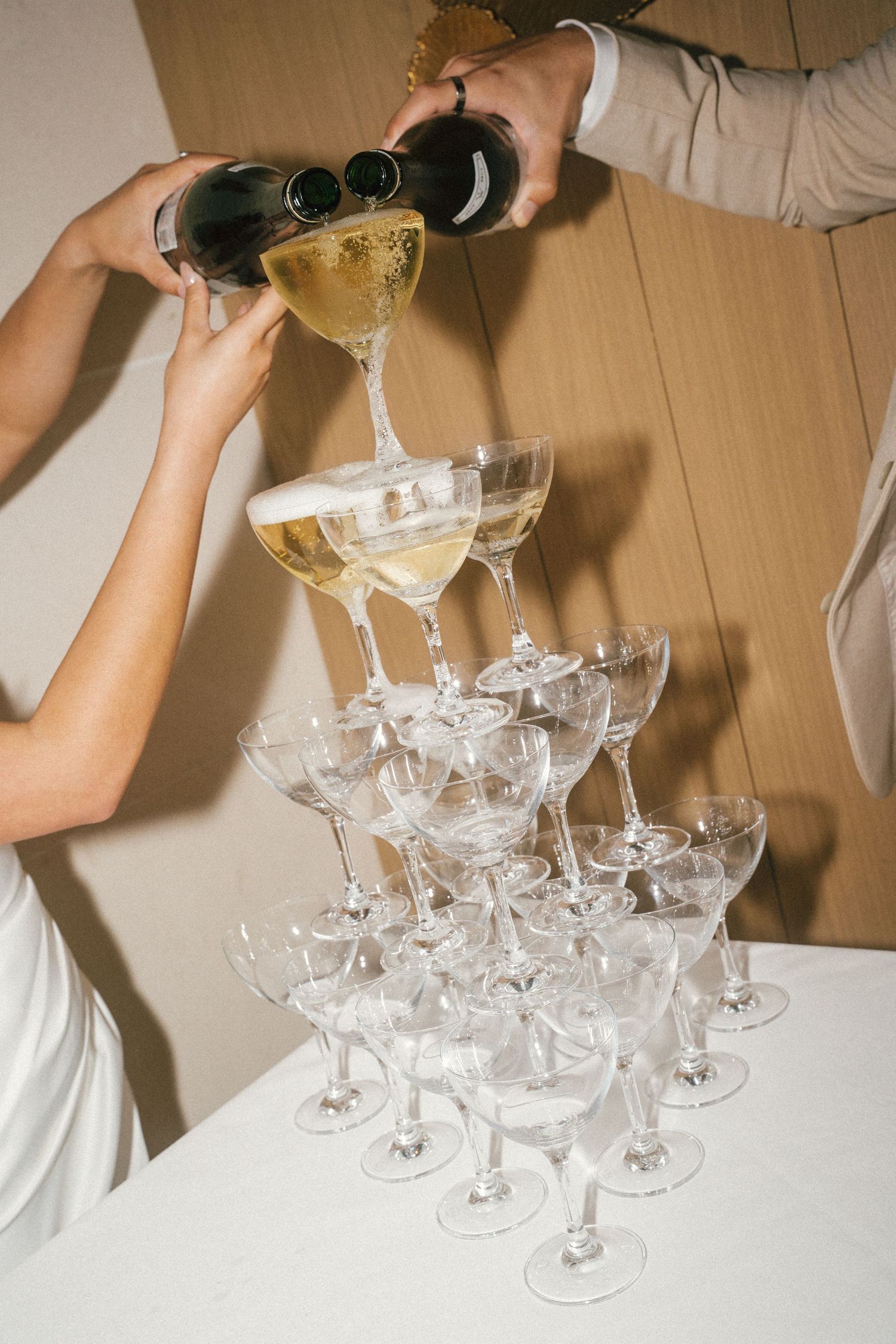 Champagne being poured into a tower of elegant crystal coupe glasses at a wedding reception.