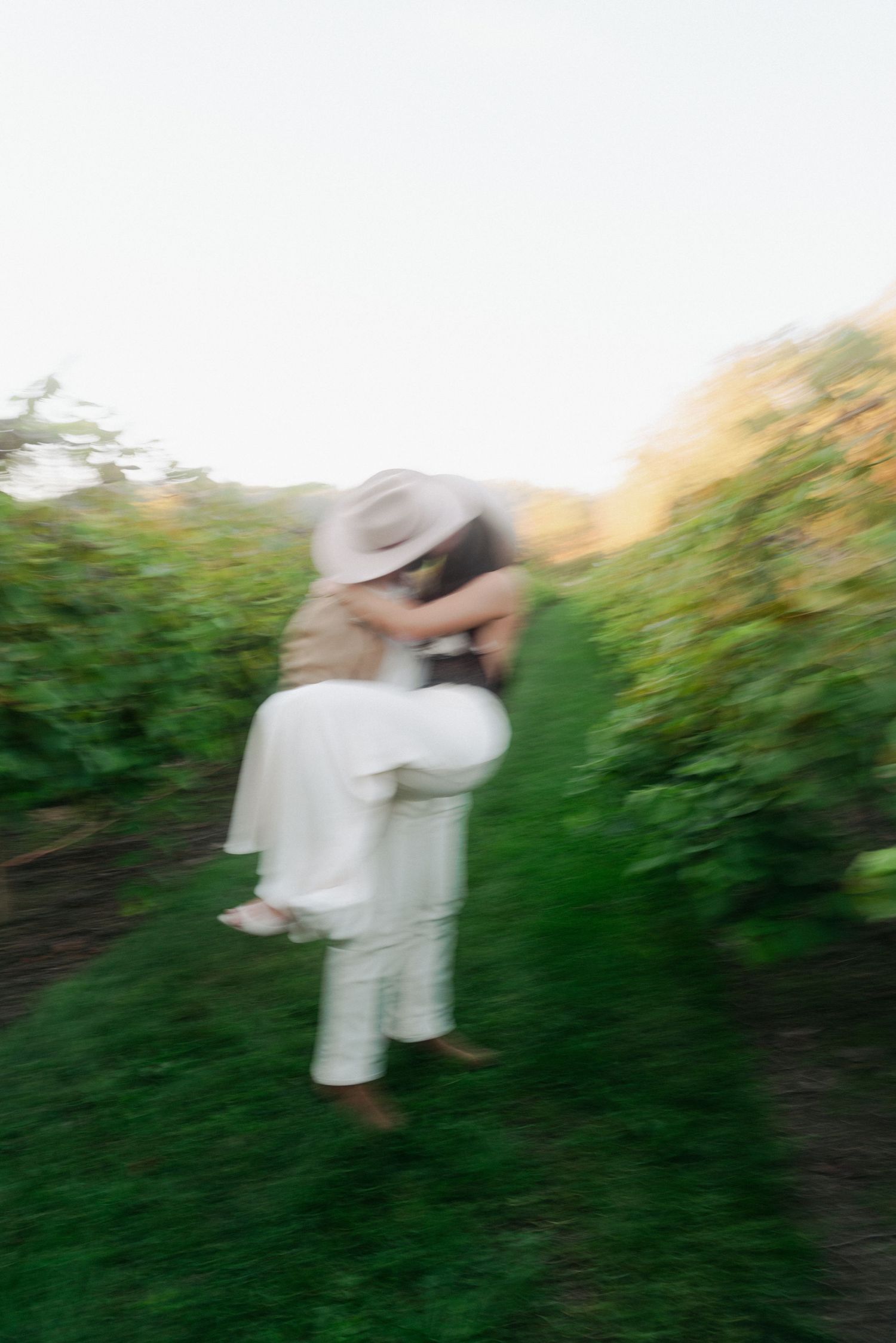 Couple embracing romantically in a lush vineyard, captured with dreamy motion blur effect.
