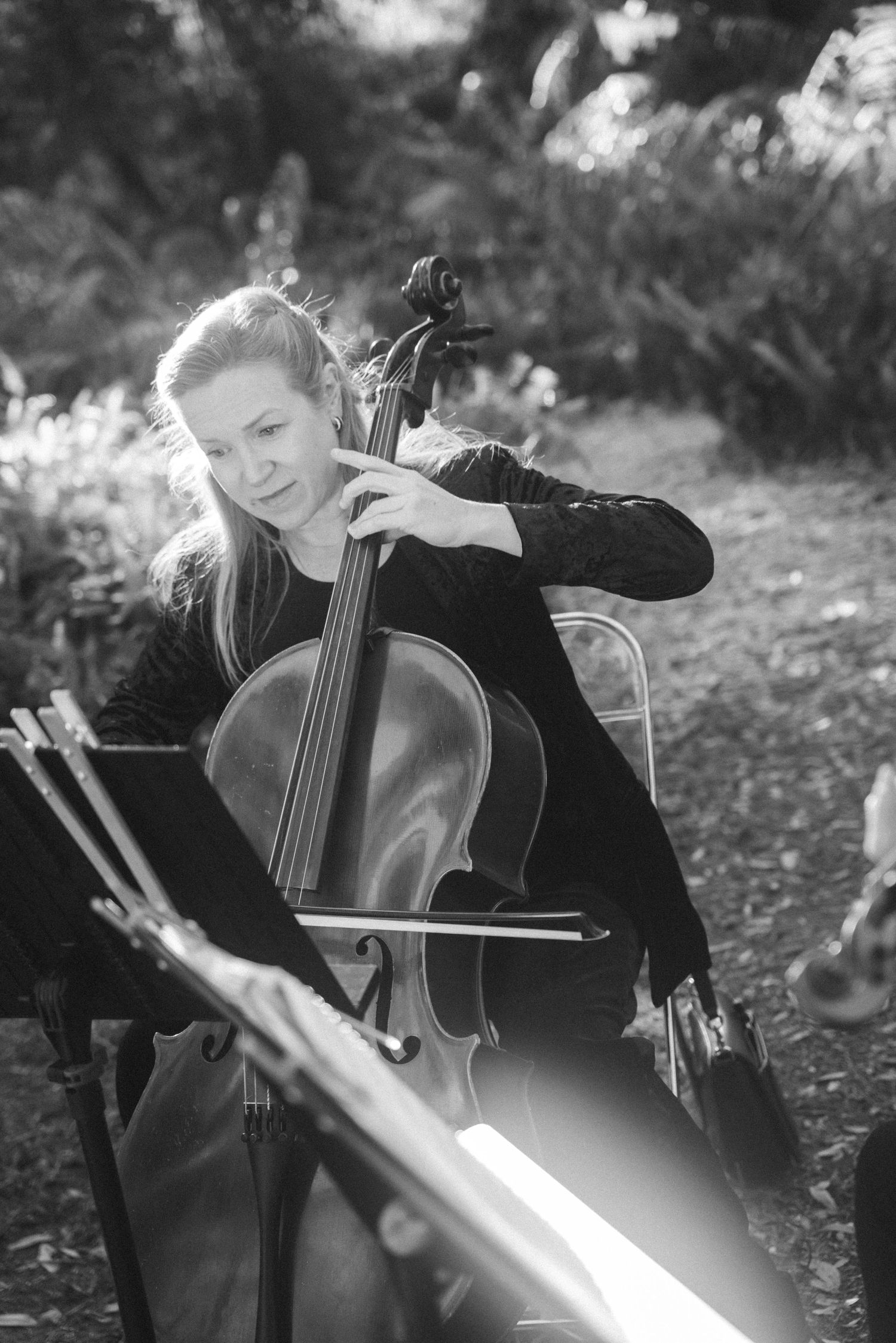 A cellist performs outdoors in an artistic black and white composition.