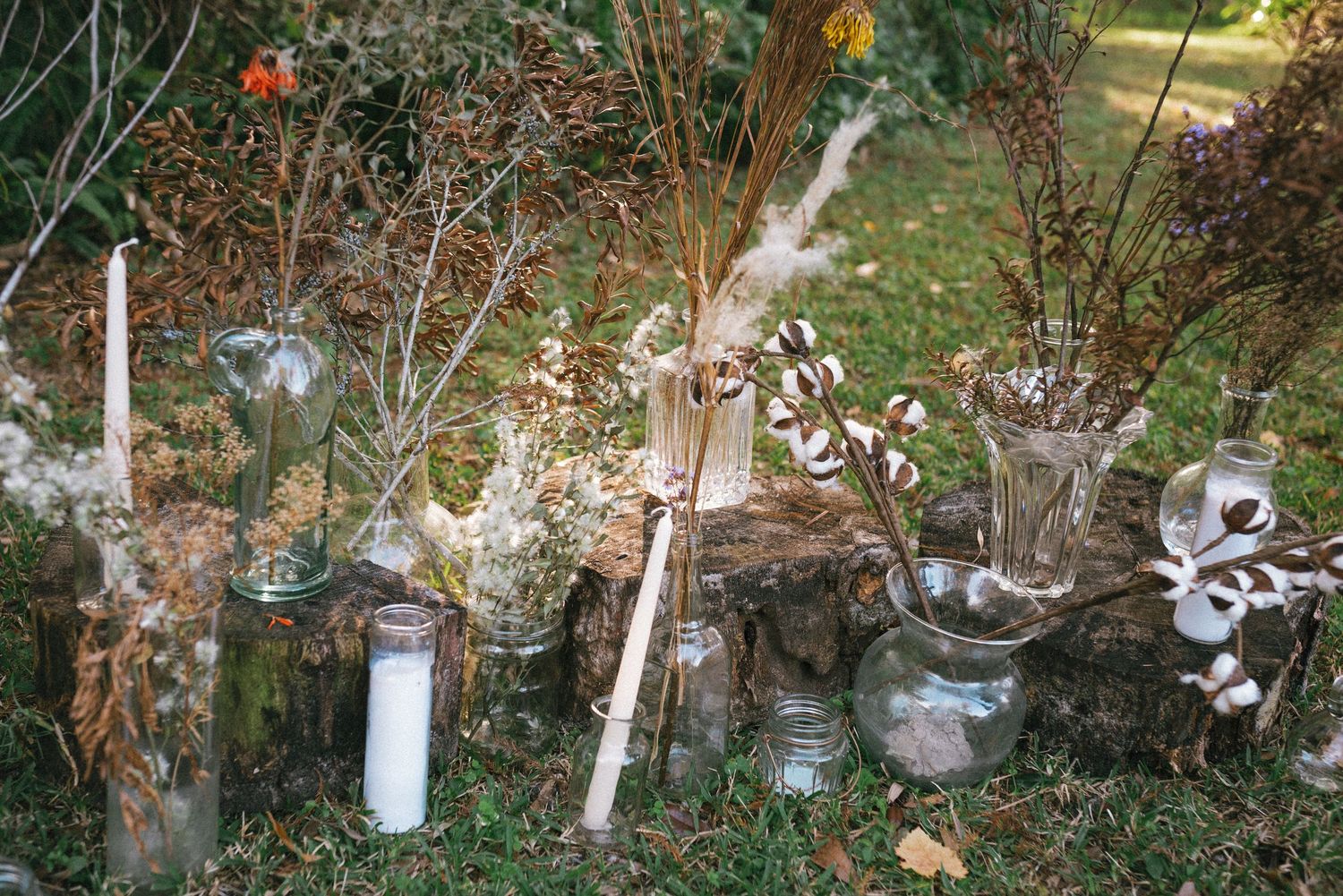 Rustic garden decor with glass jars, candles and dried flowers arranged on natural stone.