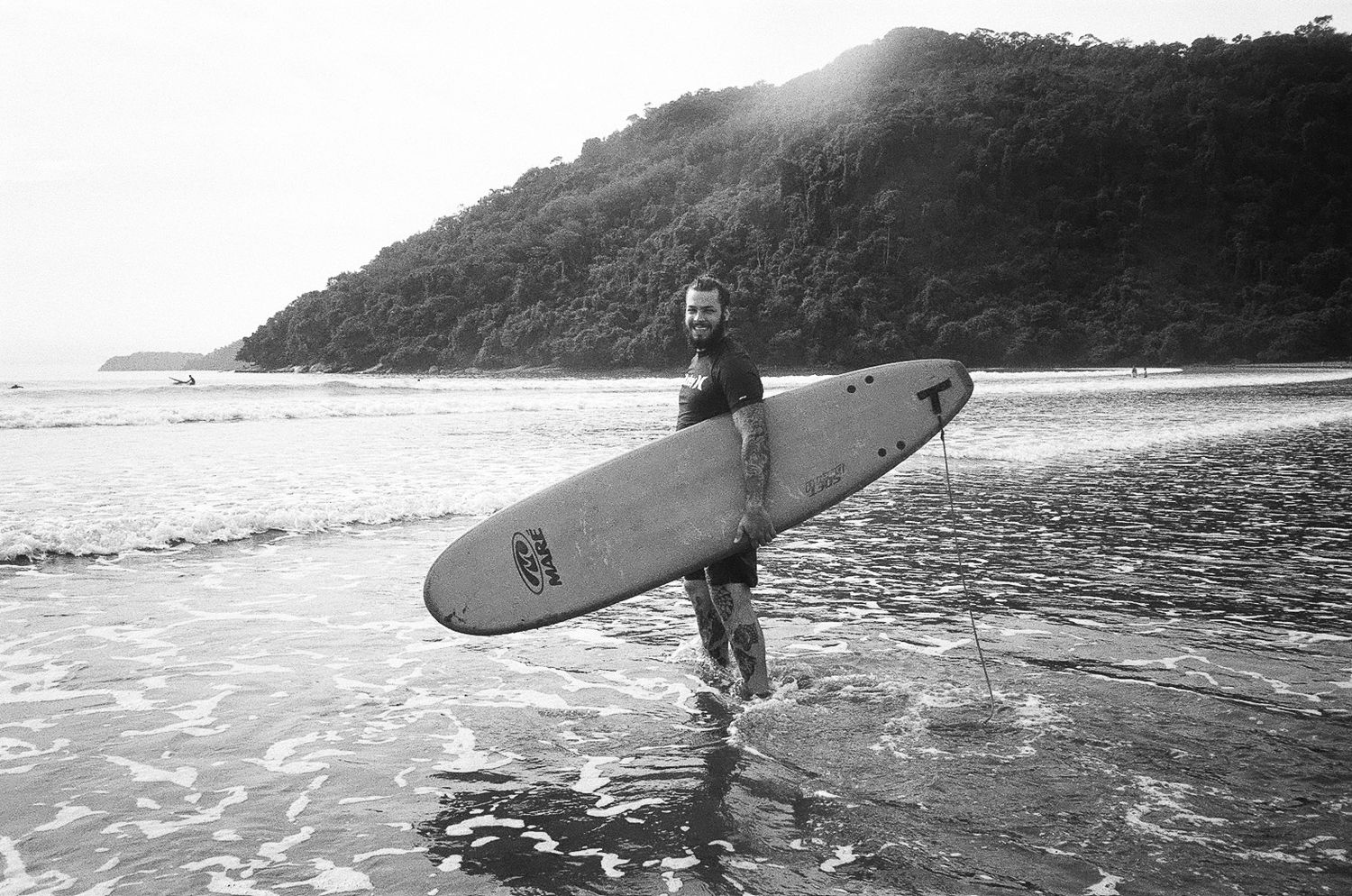 Silhouetted surfer carrying board along scenic coastal shoreline in Brazil.