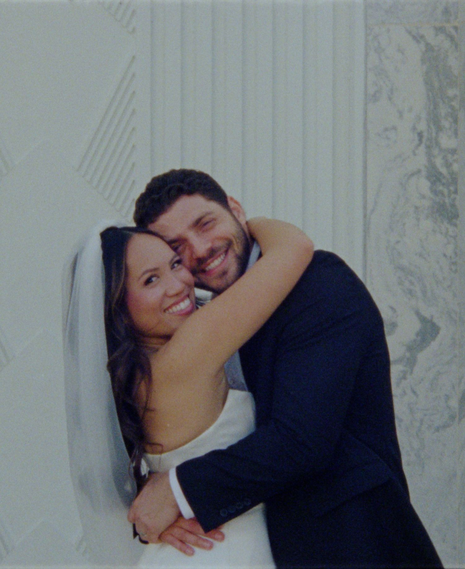 Happy bride and groom embracing and smiling on their wedding day, wearing white dress and navy suit.