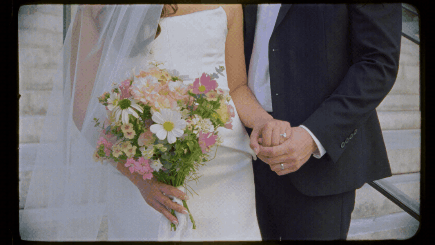 Bride and groom holding hands, bride carrying a bouquet of pink and white flowers at an outdoor wedding ceremony.