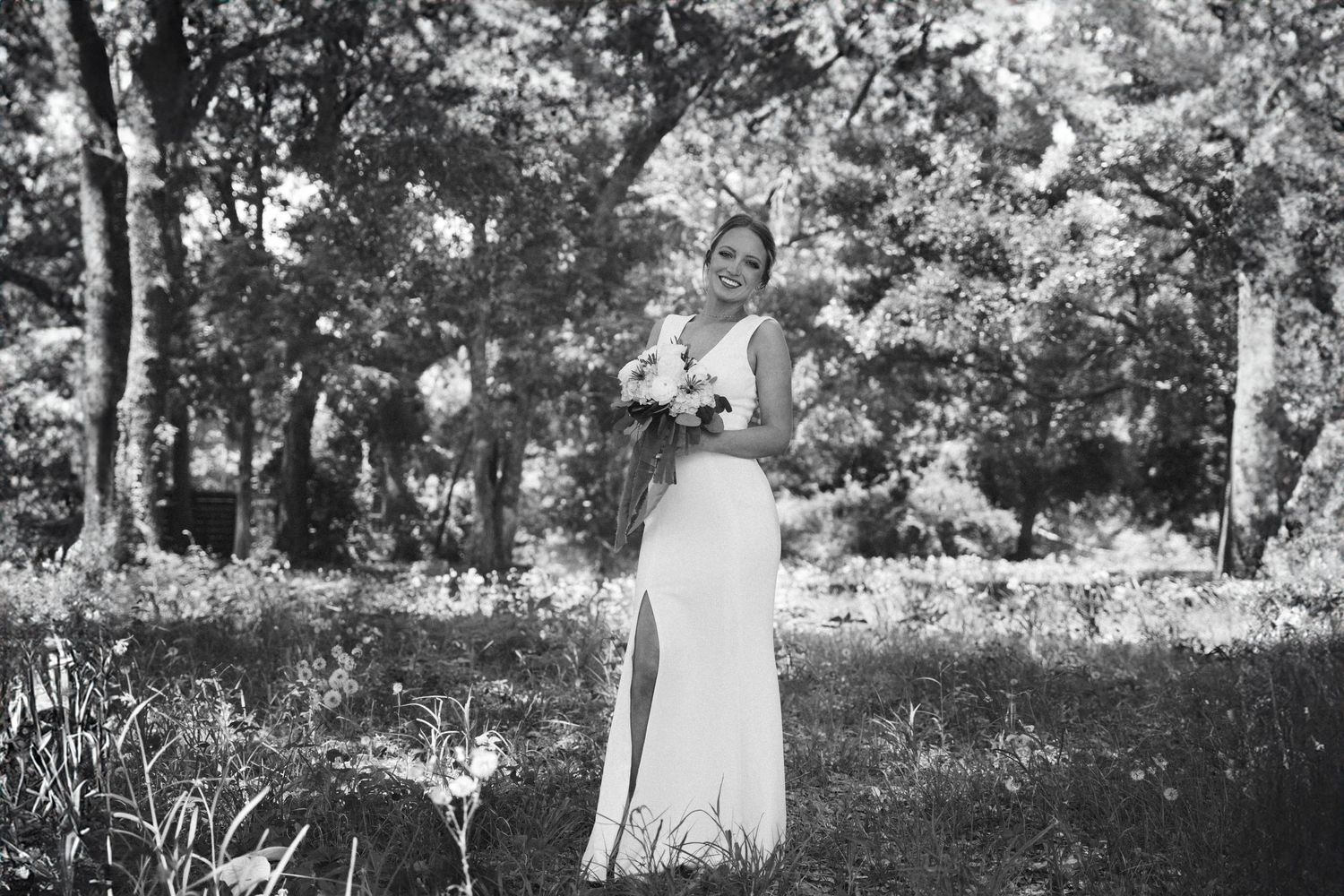 Black and white portrait of a bride holding a bouquet in a garden setting.