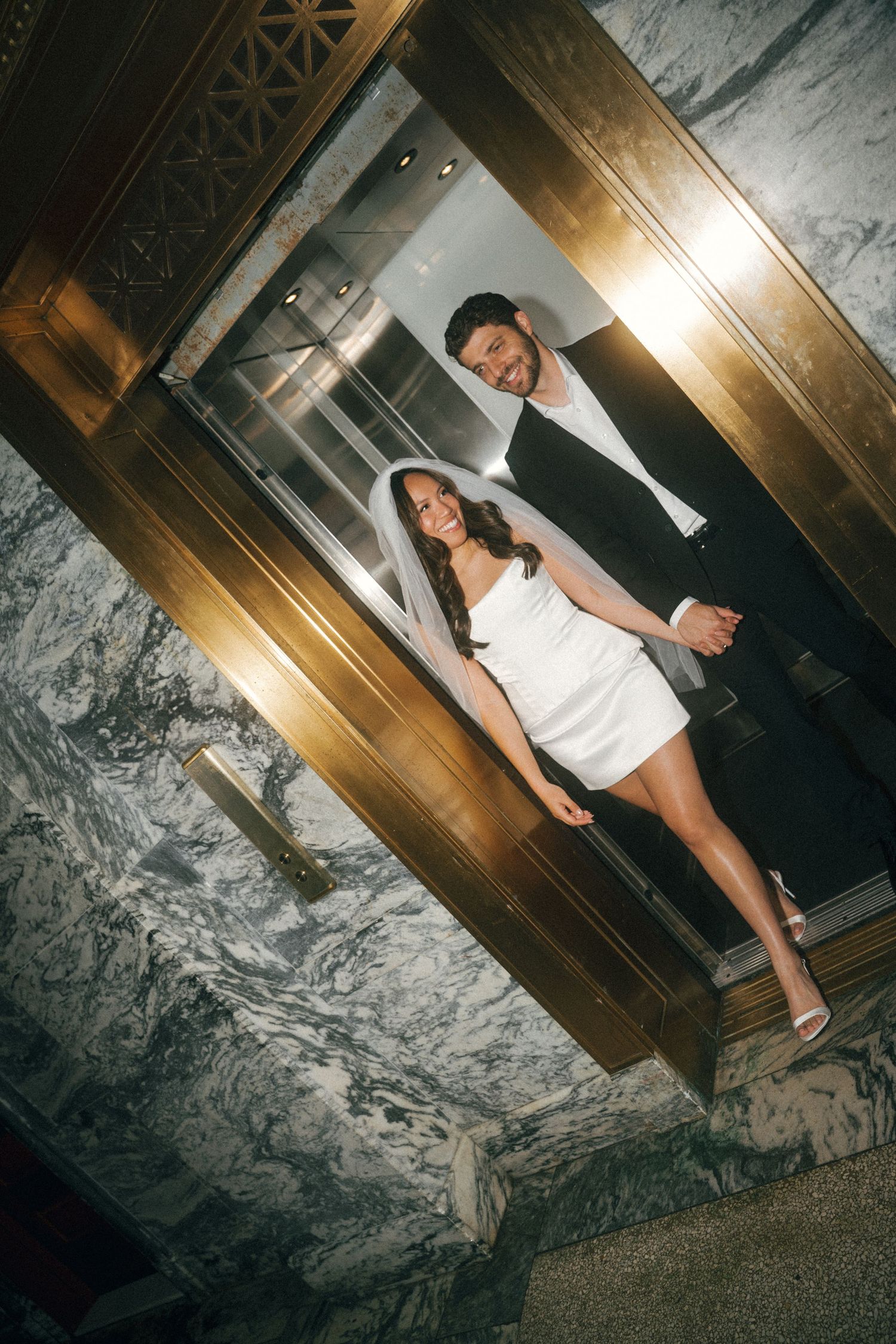 A couple poses in a dimly lit hallway with marble walls and wooden accents.