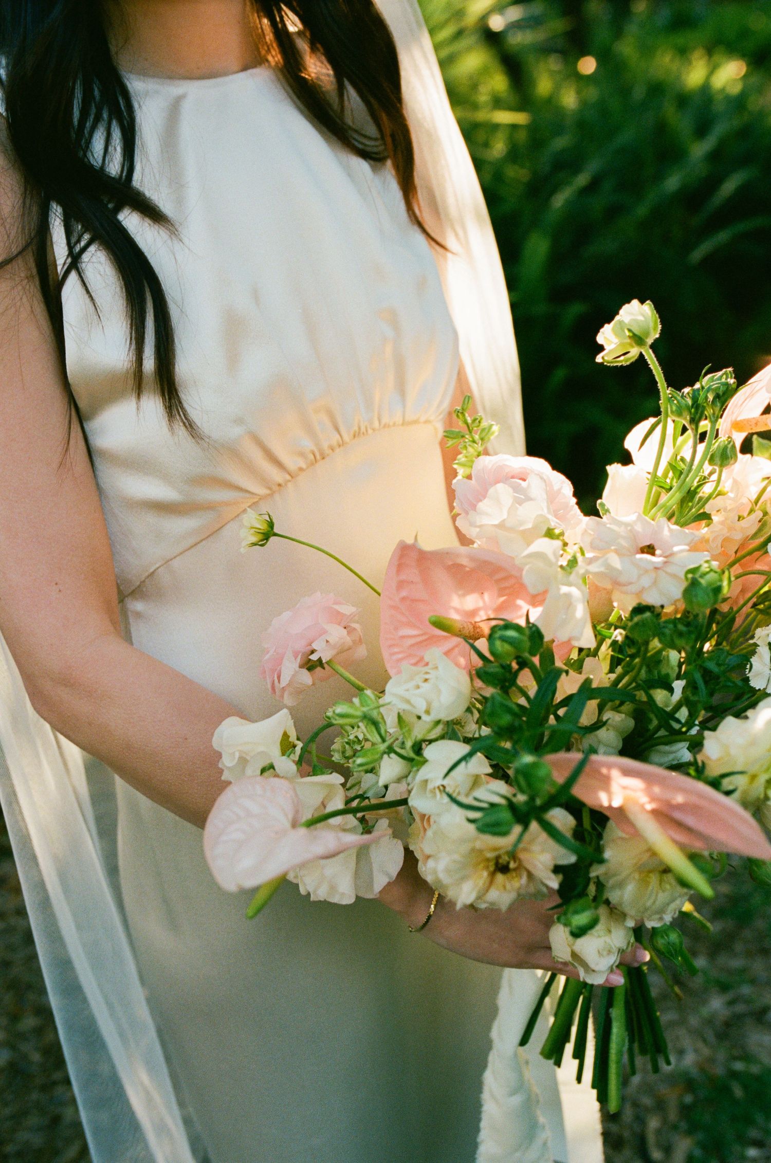 A cream-colored wedding dress detail with a soft pink and white floral bouquet.