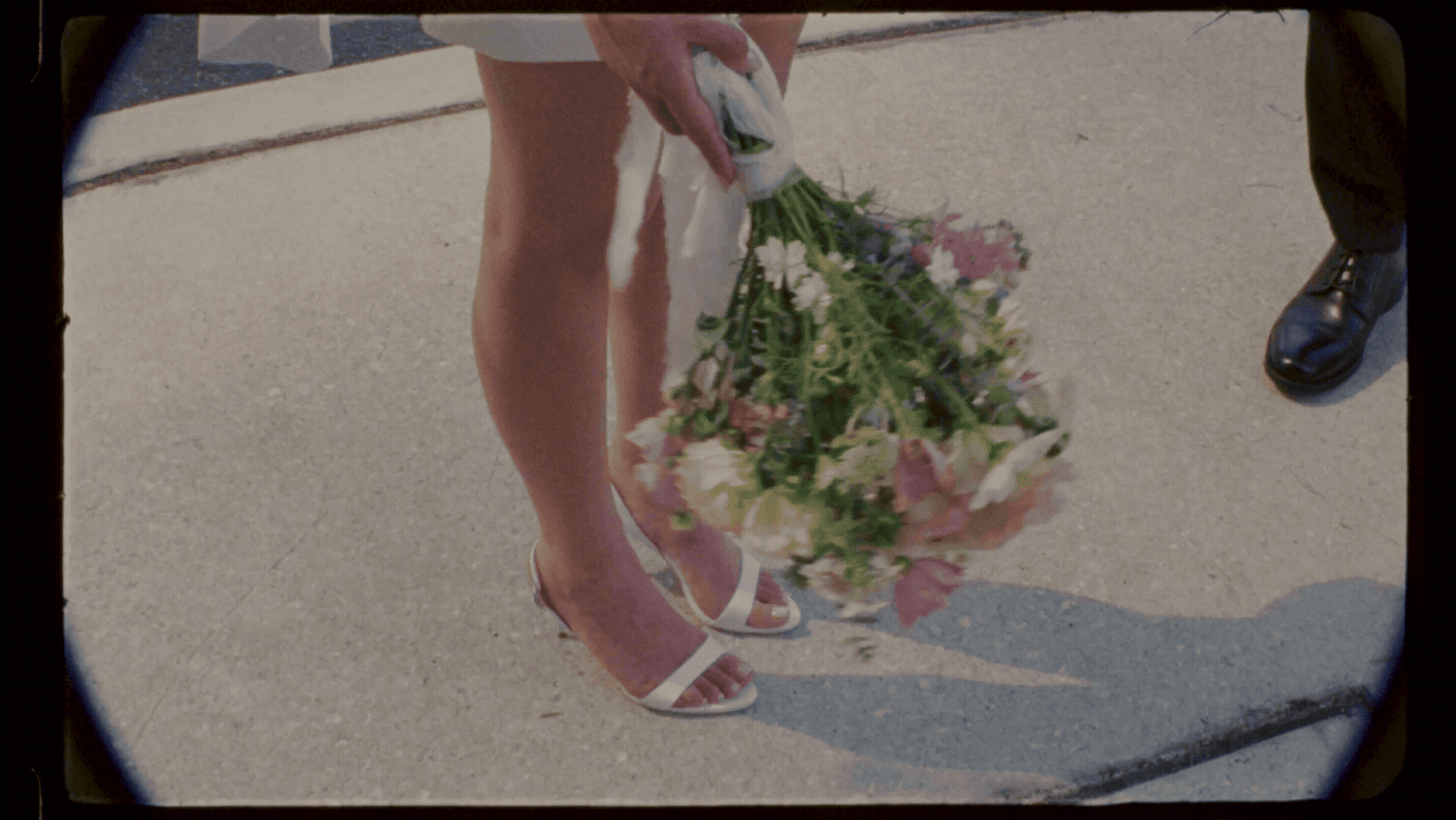 Close-up of a bride holding a floral bouquet in white heels on a sunny day.