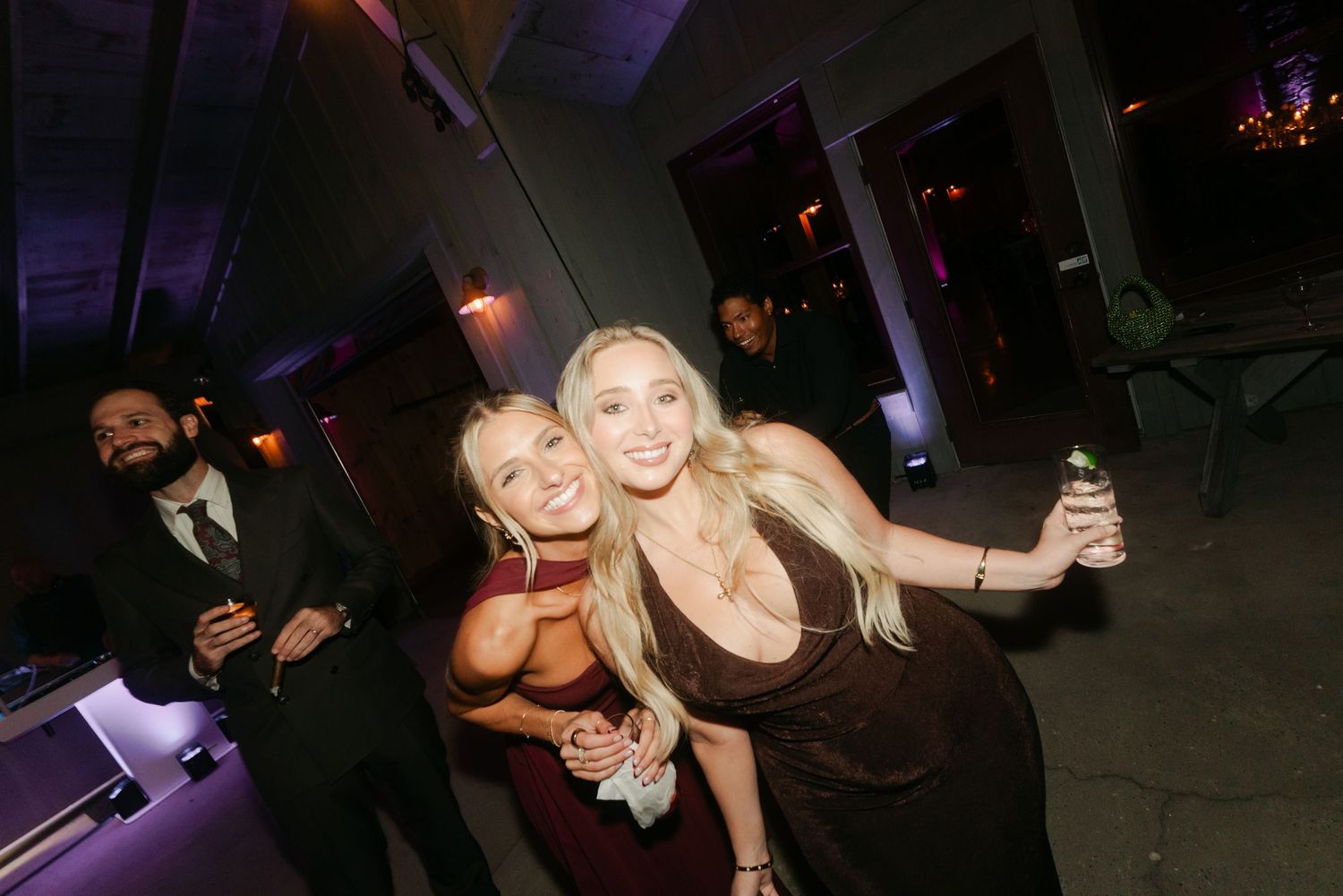 Two blonde women pose and smile together at an elegant evening party event.