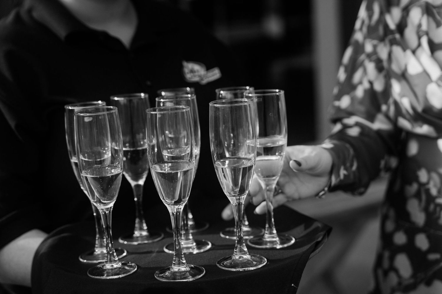 Black and white photo of champagne flutes on a serving tray at an elegant event.
