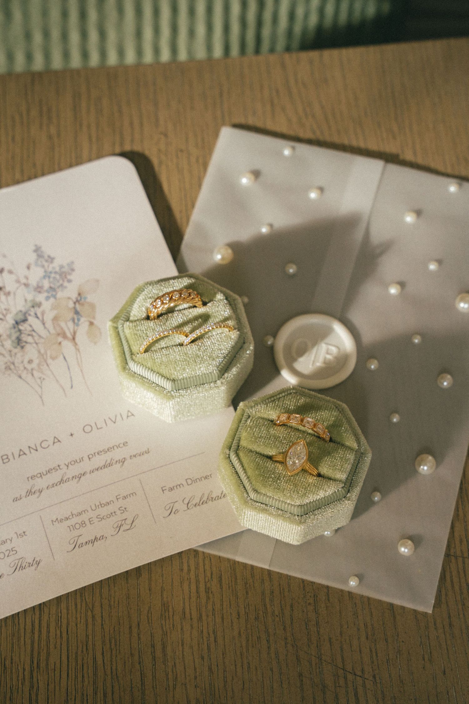 Wedding invitation cards with gold decorative boxes and pearls on wooden surface.