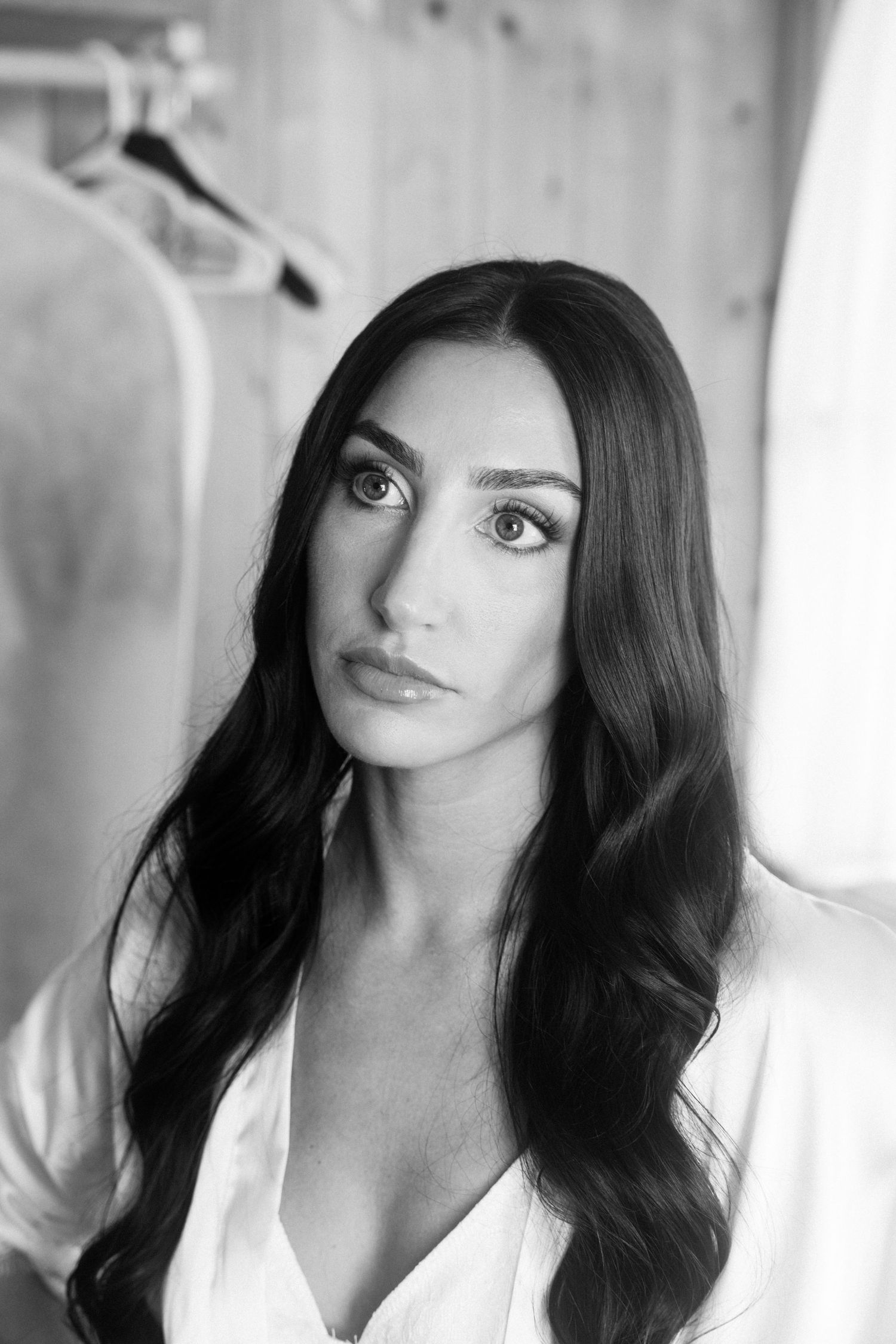 Black and white portrait of a brunette bride with long wavy hair in a white robe preparing for her wedding.