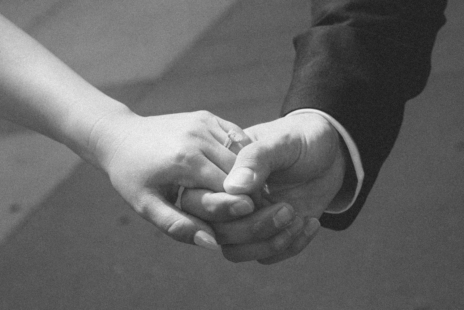 Black and white photo of a couple holding hands, with a wedding ring visible, symbolizing love and commitment.