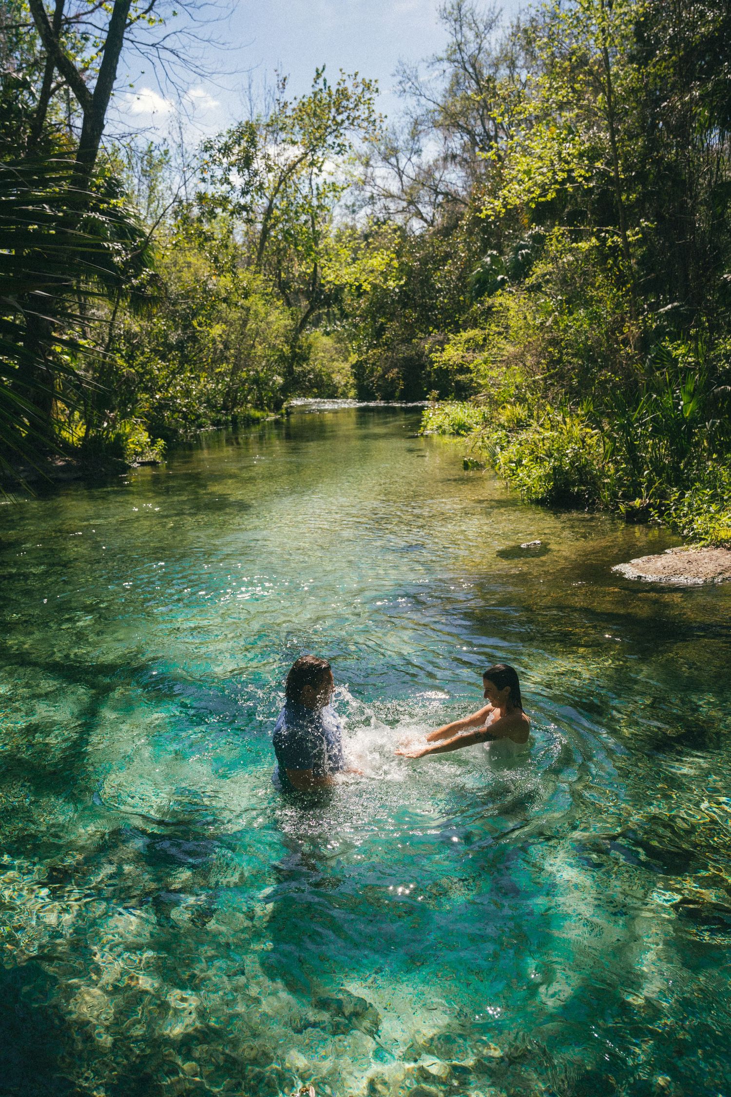 Couple swimming in a pristine natural Florida spring with emerald green waters and surrounding foliage.