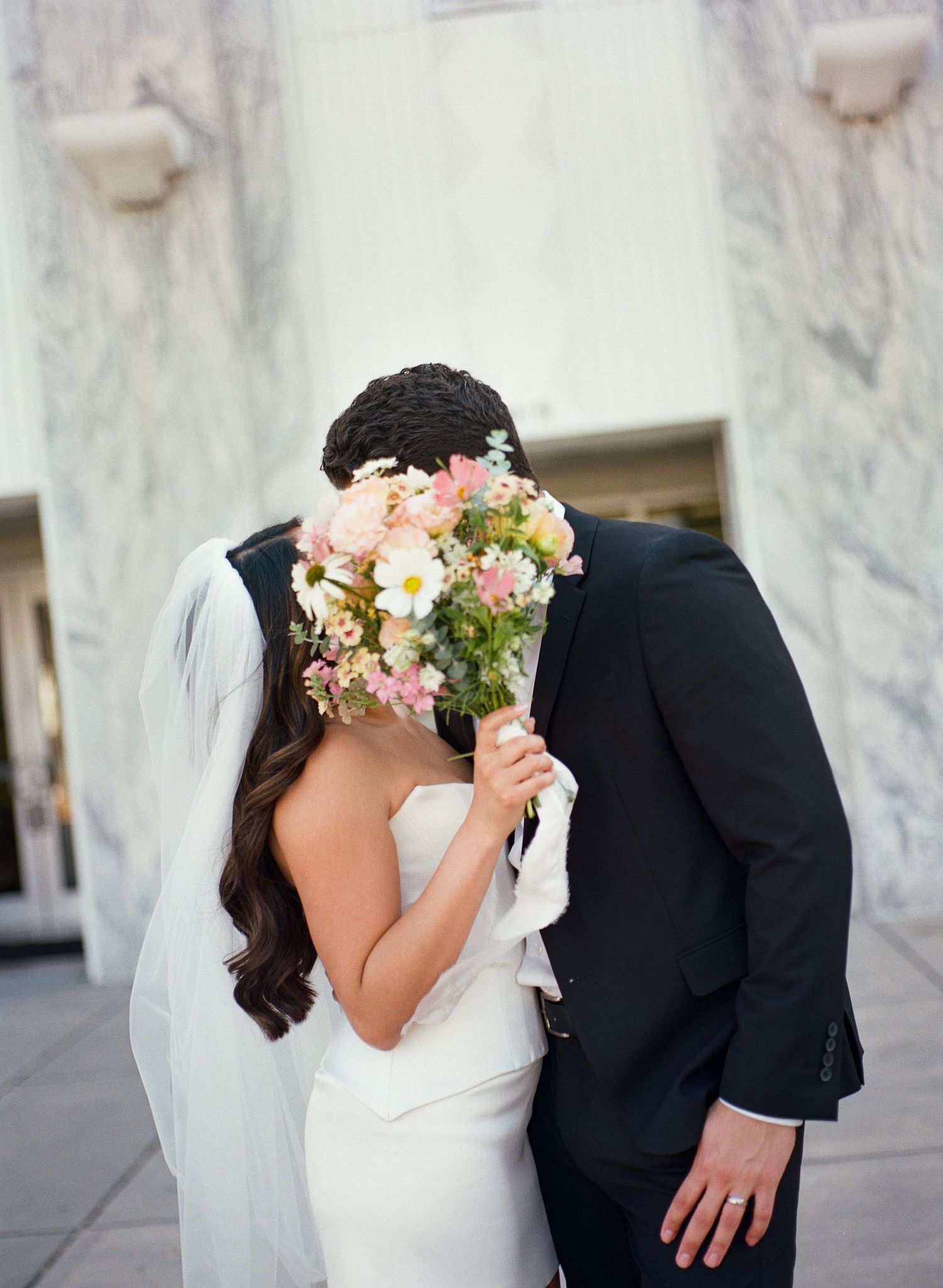 Wedding couple in black and white sharing an intimate moment against a marble wall.