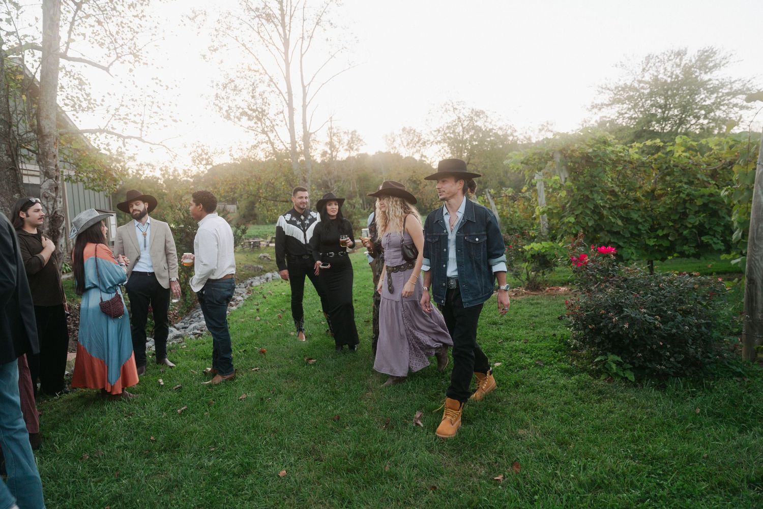 Group of stylishly dressed guests enjoying an outdoor garden party at golden hour.