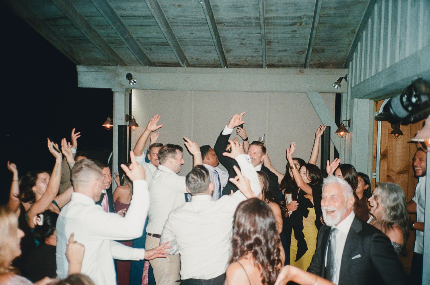 Energetic wedding reception dance floor with guests raising their hands during celebration.