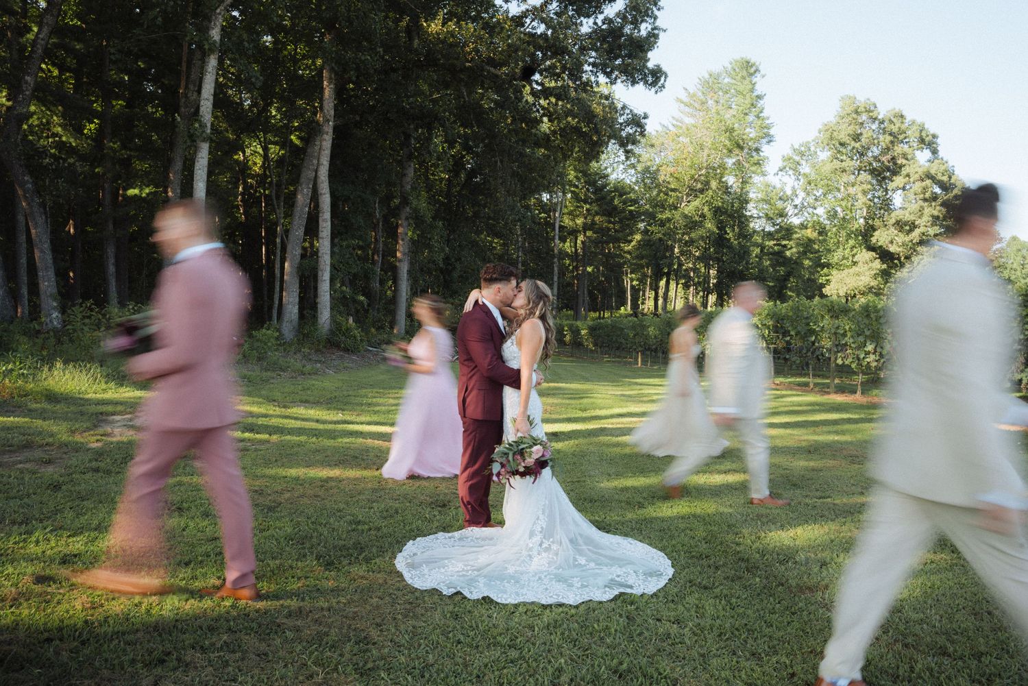 Artistic shot of wedding guests moving around stationary couple in wooded setting.