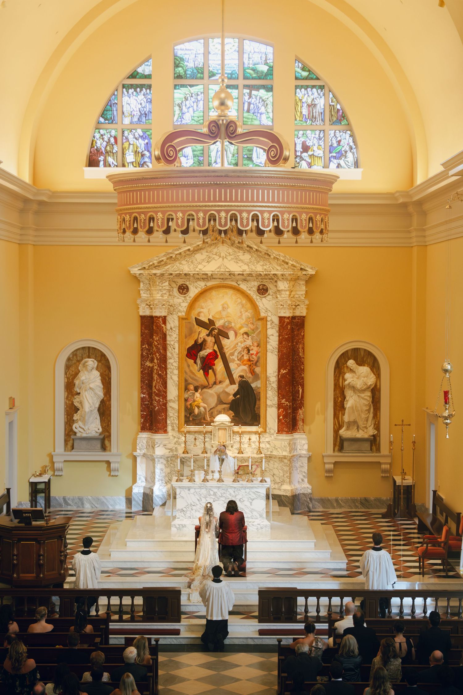 Interior of an ornate Catholic church with yellow walls and white marble altar.