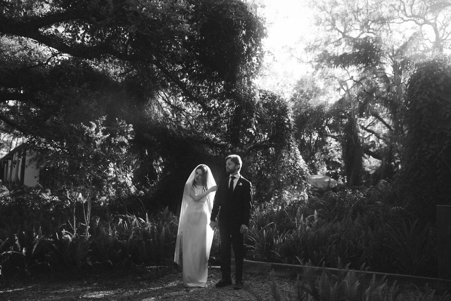 Black and white wedding photos showing couple walking through a natural garden setting.
