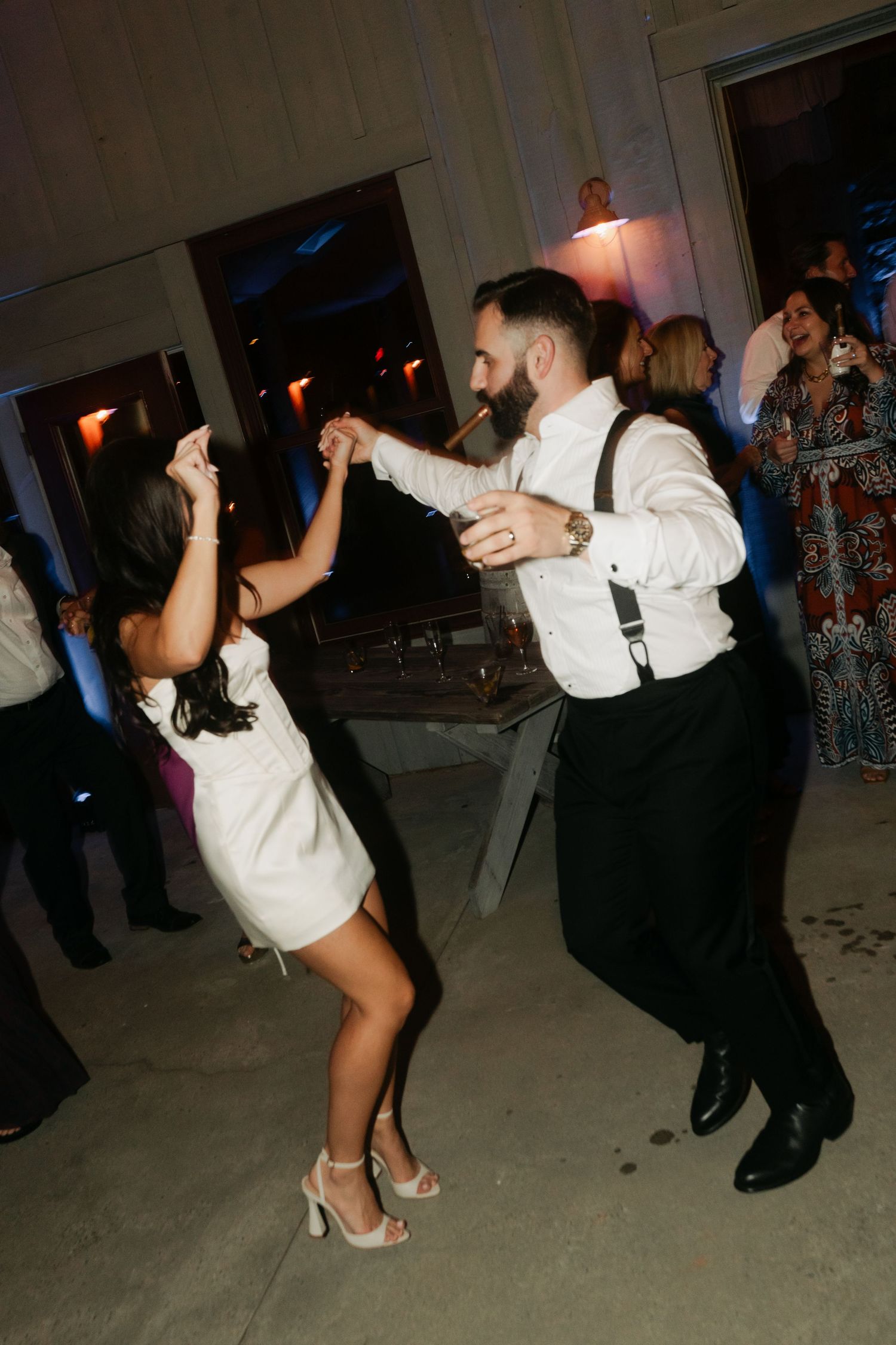 Couple dancing energetically at a wedding reception, man in suspenders twirling woman in white dress.