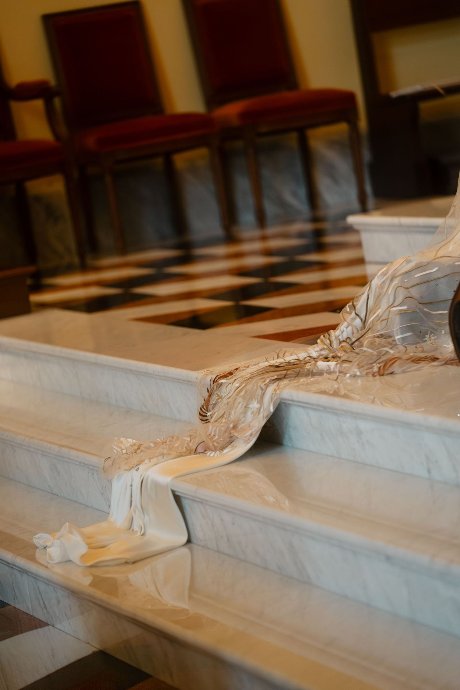 Elegant marble altar steps with draped white fabric in a formal hall with checkered floors and red chairs.