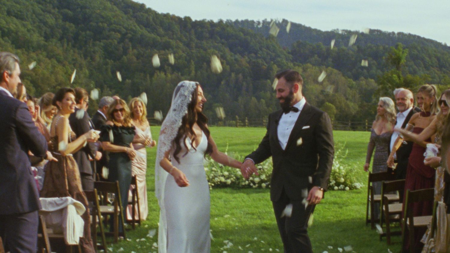 Wedding celebration in a scenic mountain meadow with guests throwing flower petals.