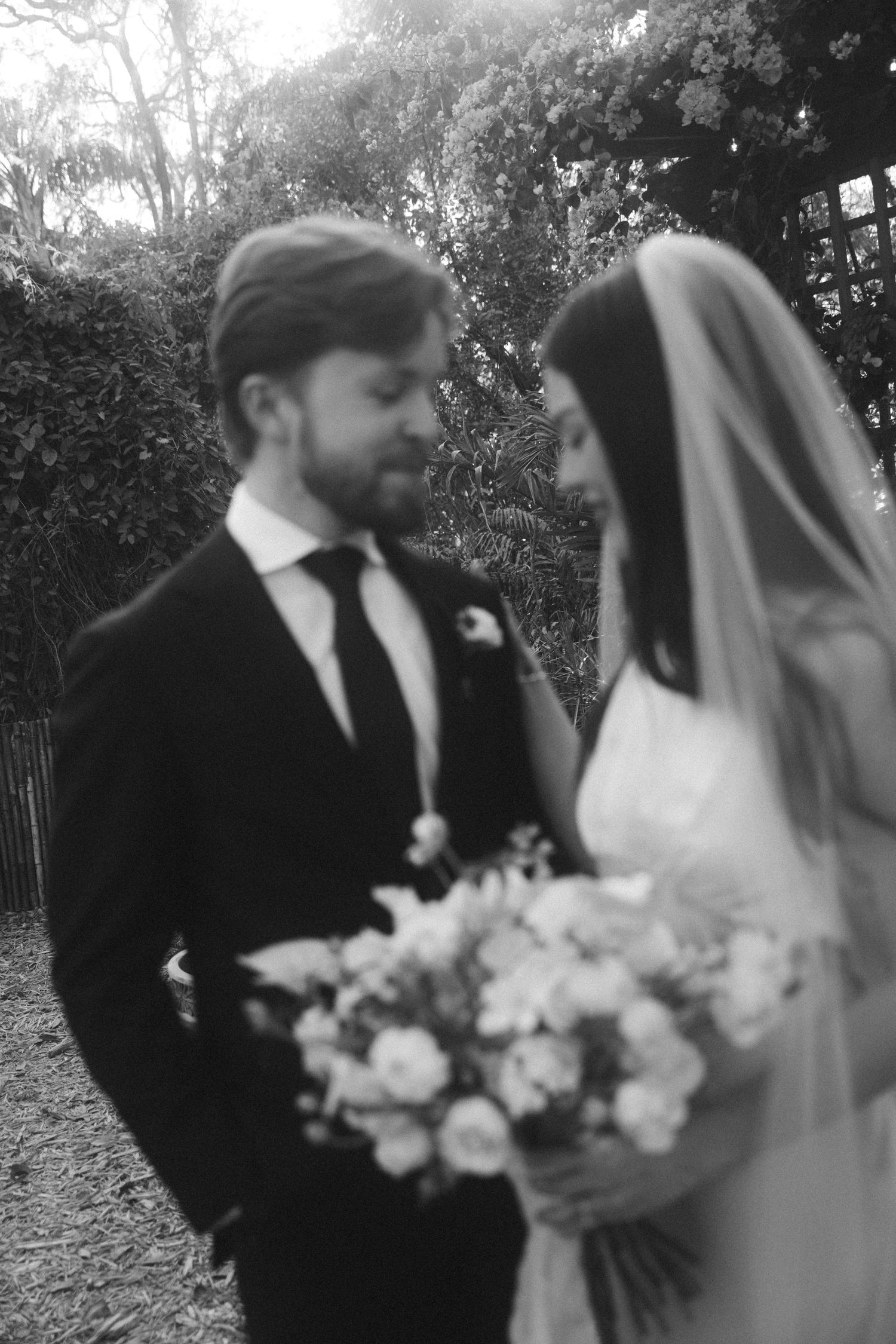Black and white wedding portraits showing couple with elegant floral bouquet in garden setting.