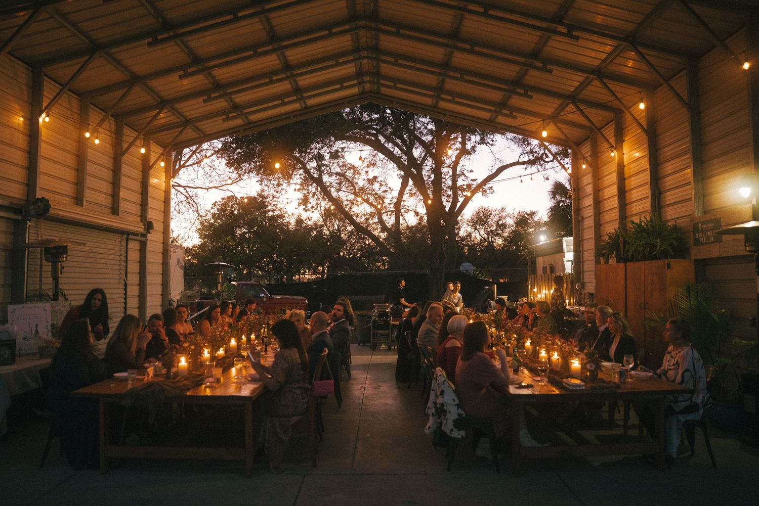 Panoramic view of an outdoor wedding reception venue at sunset with ambient lighting.