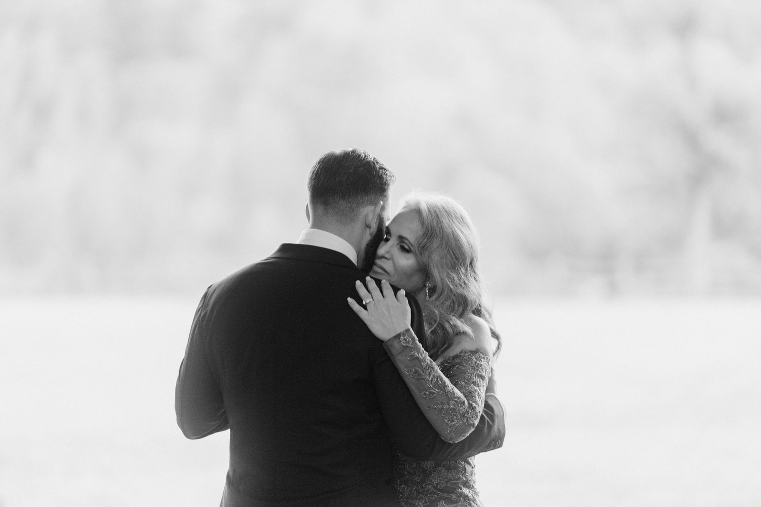 Black and white photo of couple embracing tenderly in an open field at a wedding.