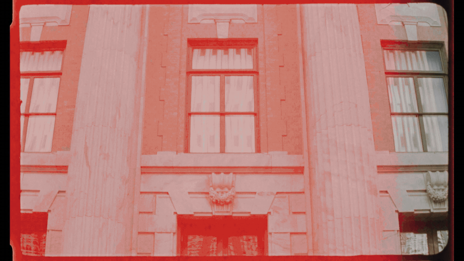 Red-tinted vintage photo of a classic brick building facade with tall windows and ornate stone columns.