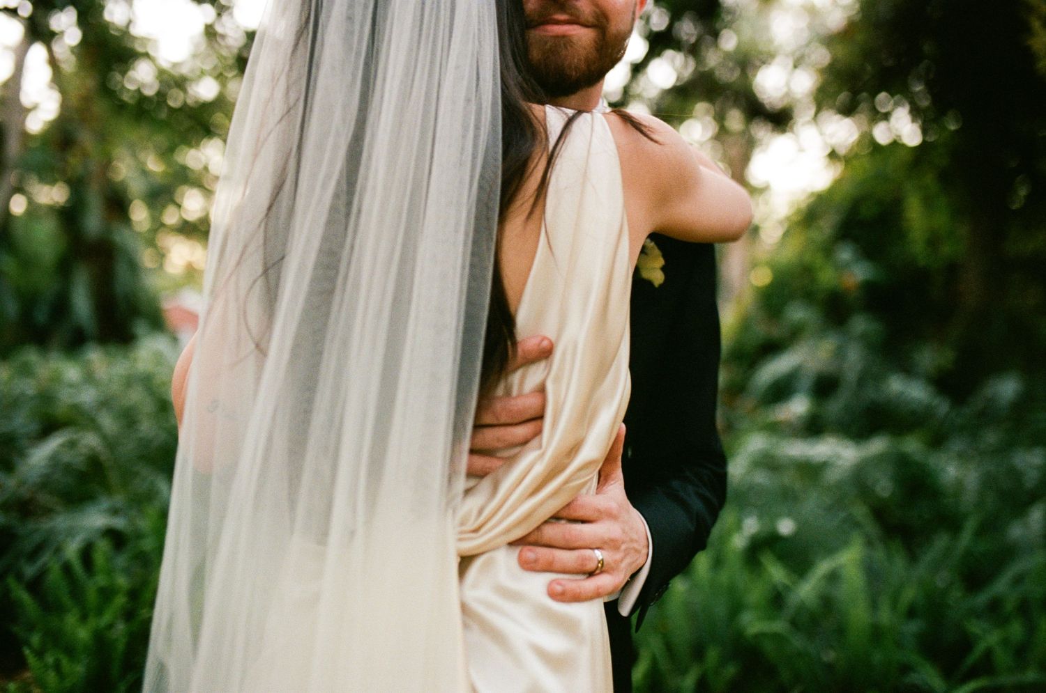 A tender embrace between newlyweds in an outdoor garden setting.