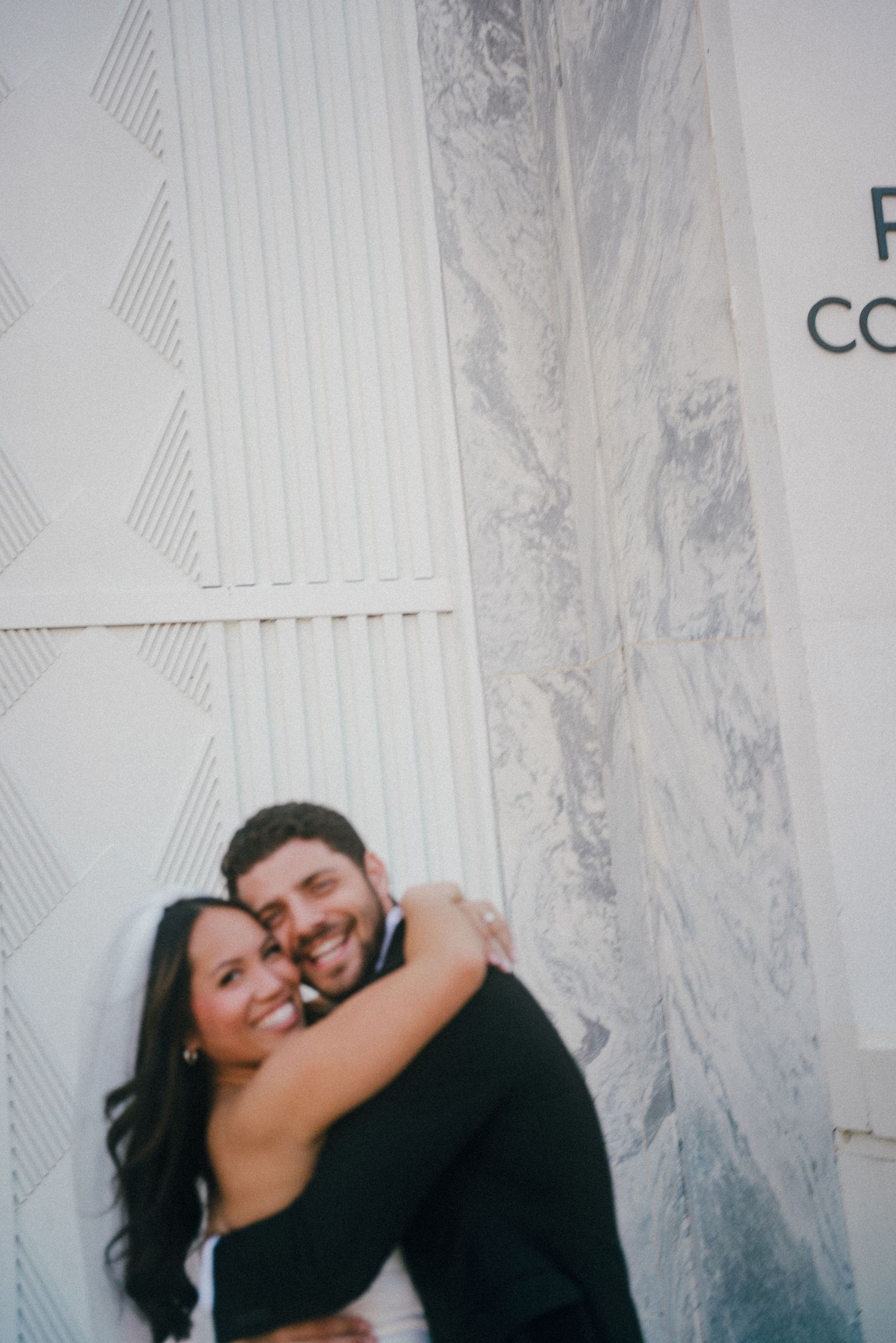 A couple shares an intimate moment against a textured white wall.