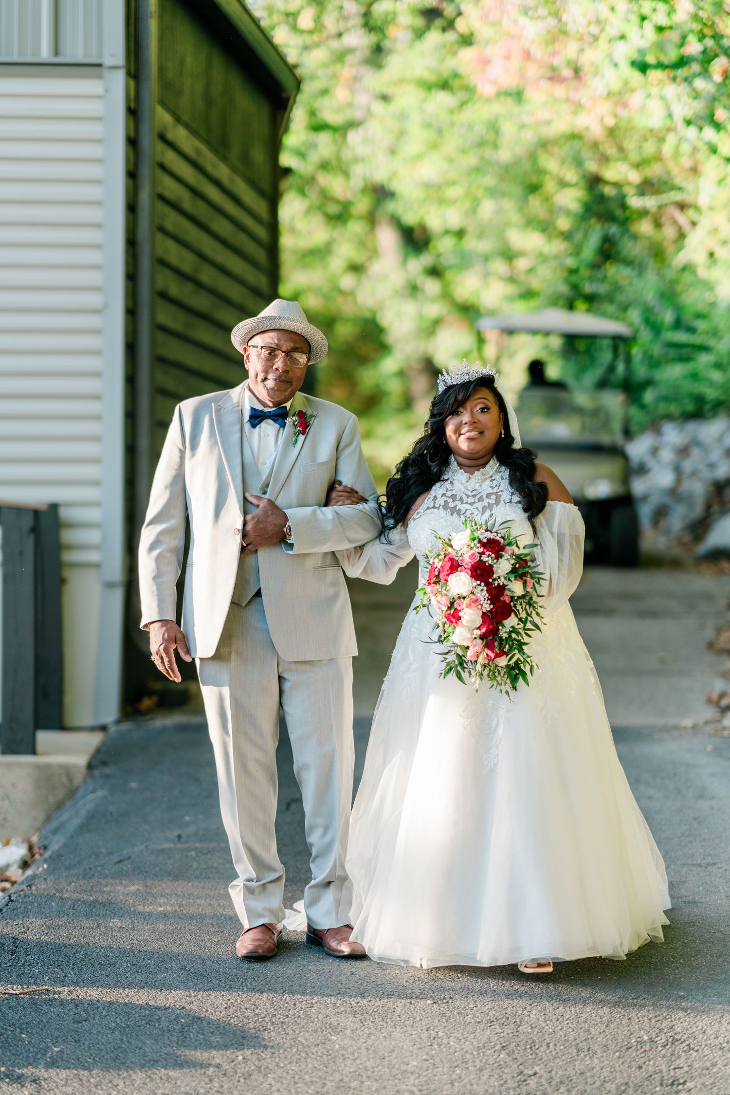 A bride in white holds a floral bouquet while walking with an elder in a light suit.