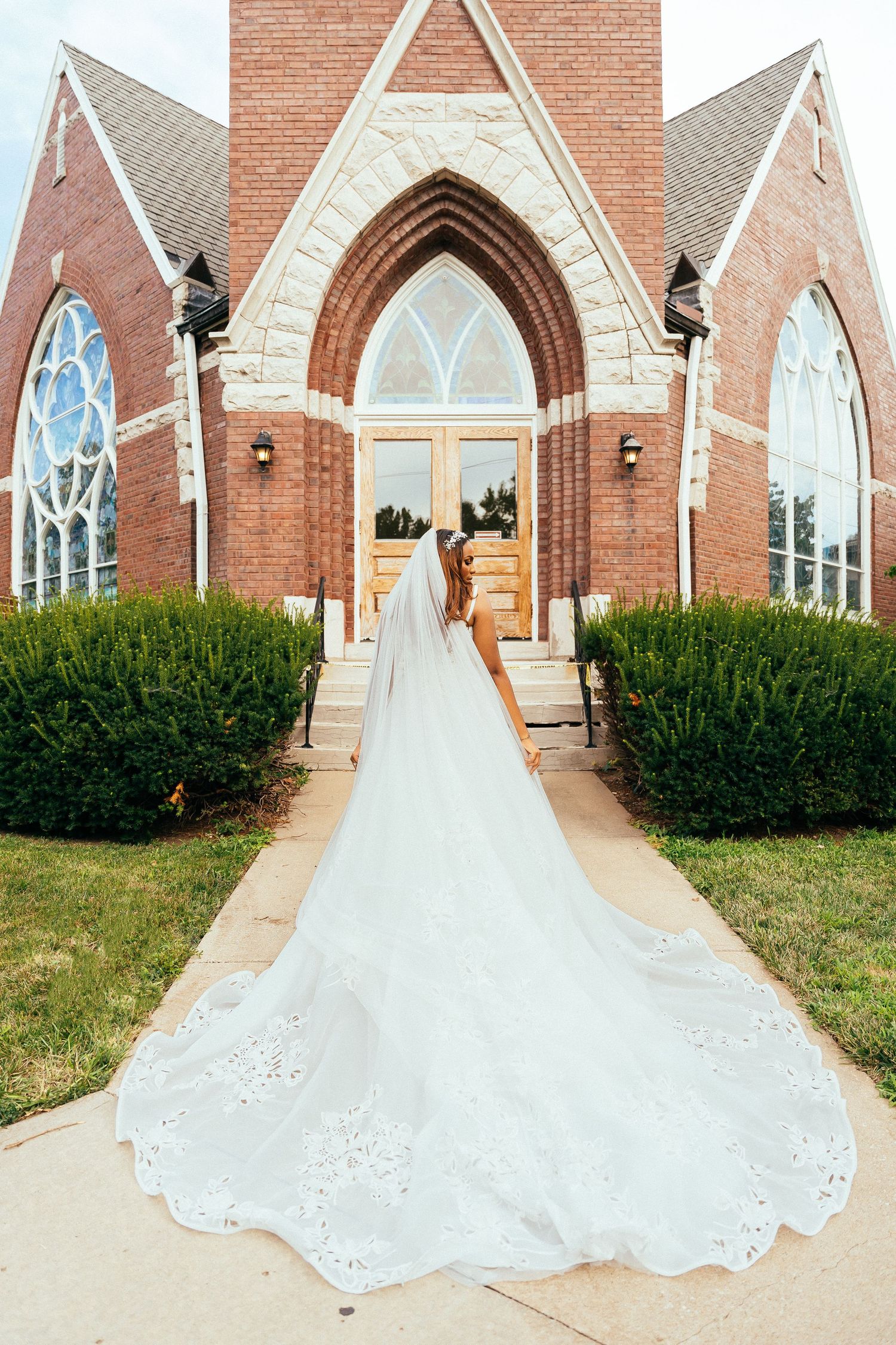 A bride's long train extends down church steps leading to gothic-style wooden doors.