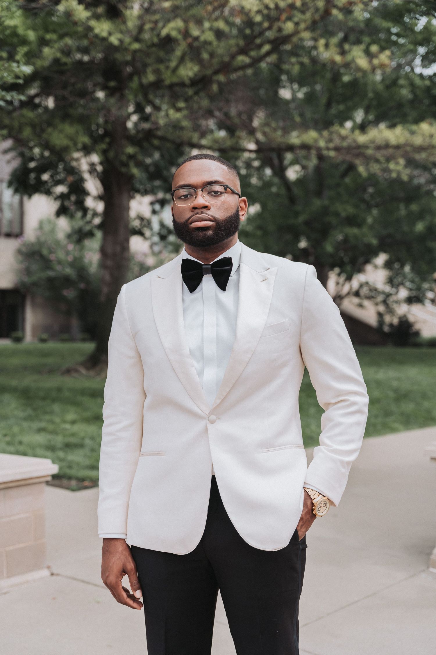 Dapper gentleman in white dinner jacket and bow tie poses outdoors.