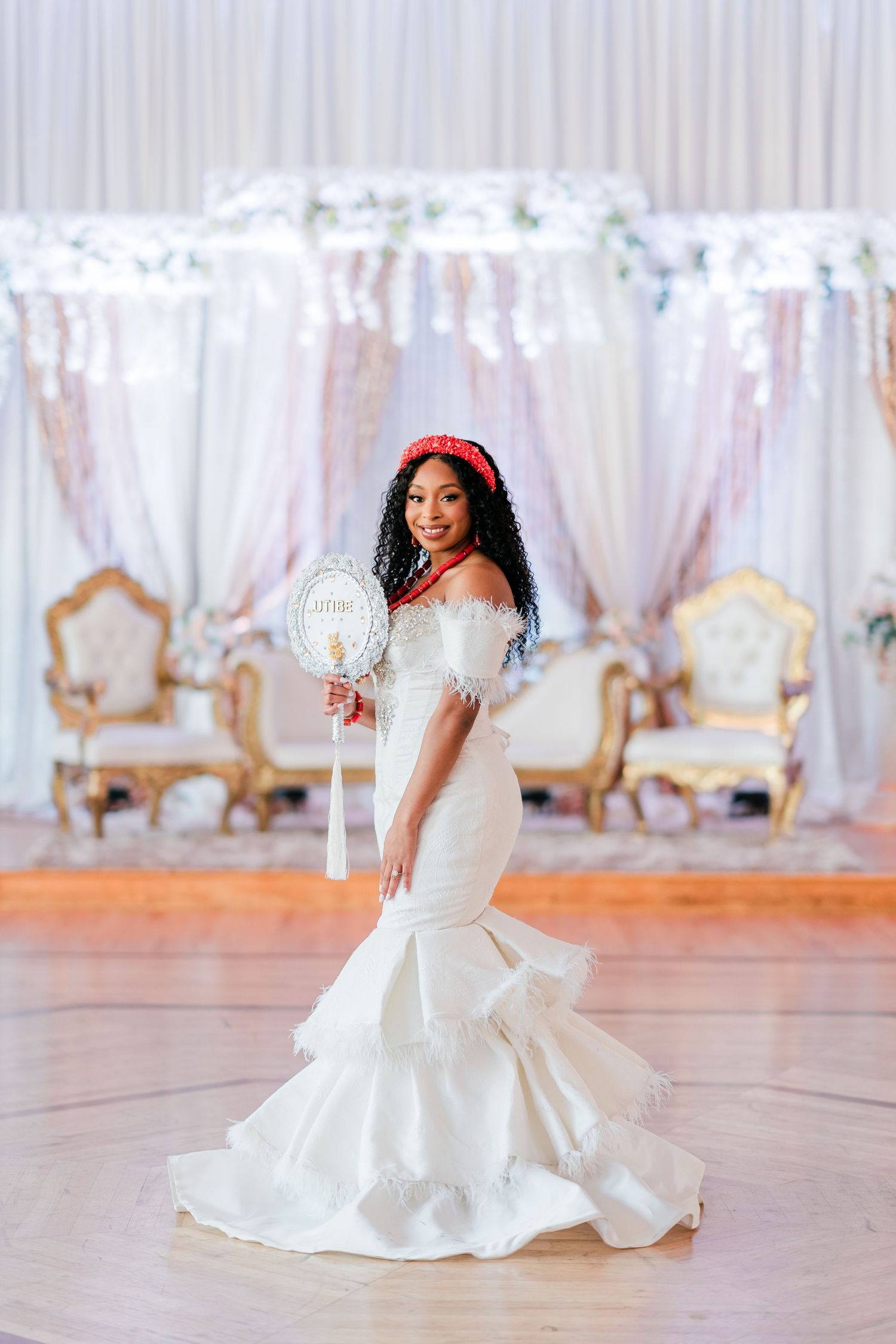 Elegant bride in a fitted mermaid wedding gown with feather details poses in front of ornate backdrop.