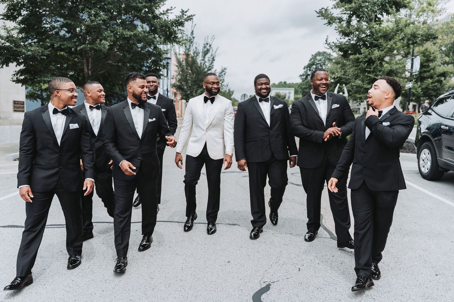 Group of groomsmen in black and white tuxedos walking and smiling outdoors.