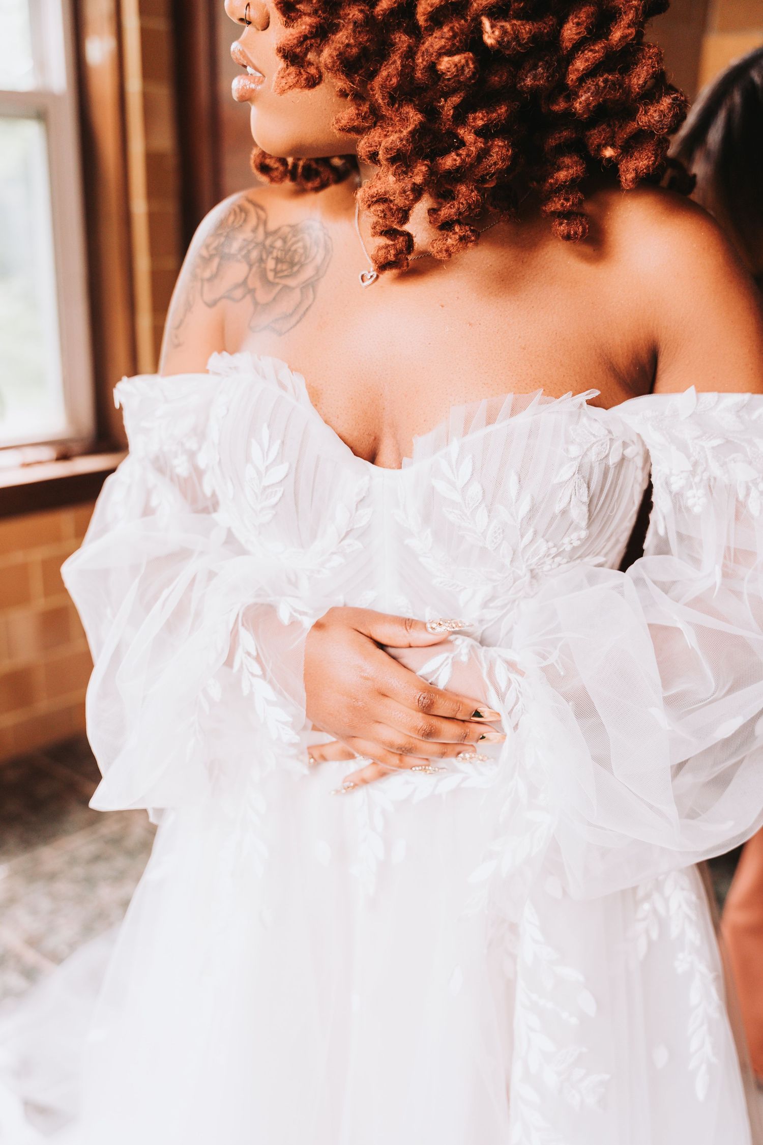 A close-up shot shows delicate white ruffled fabric of a wedding dress and an elegant shoulder tattoo detail.
